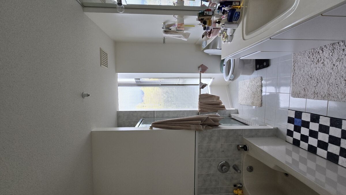 Condo bathroom before renovation — original white tile, dated vanity and fixtures, West Vancouver