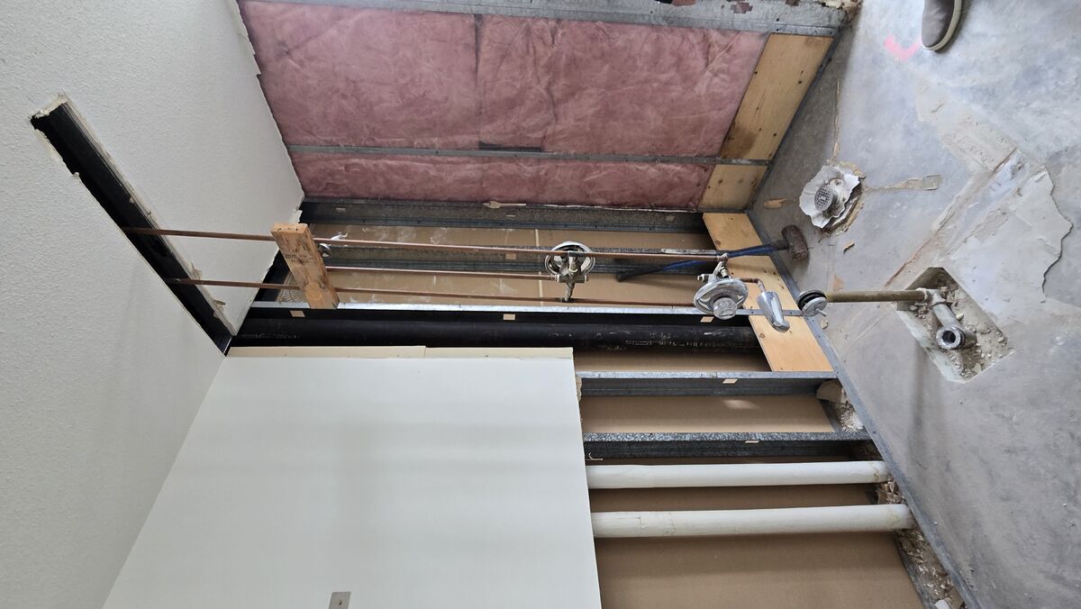 Condo bathroom during demolition — exposed steel framing, plumbing rough-in, insulation visible