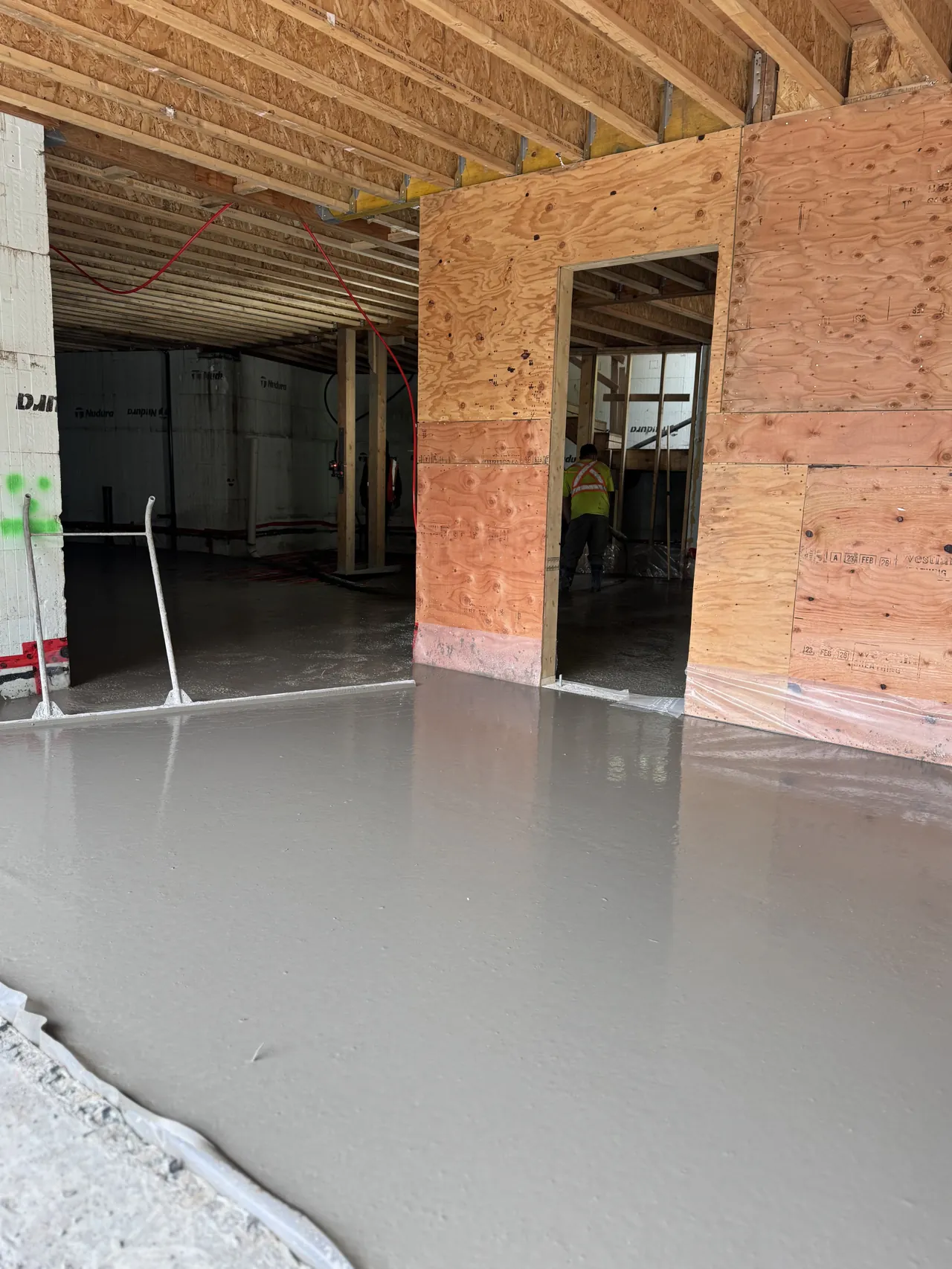 Freshly poured interior slab-on-grade inside a framed and roofed home, smoothly floated and protected from rain