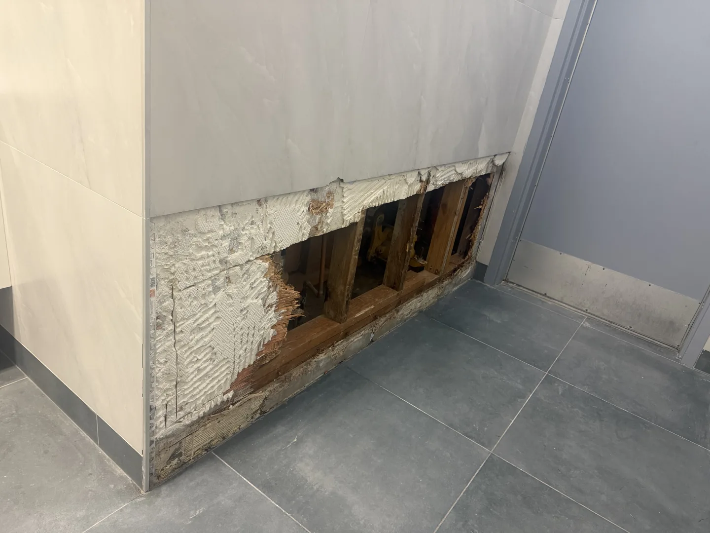 Exploratory ceiling opening at a wall interface during a strata water ingress investigation, exposing joists above