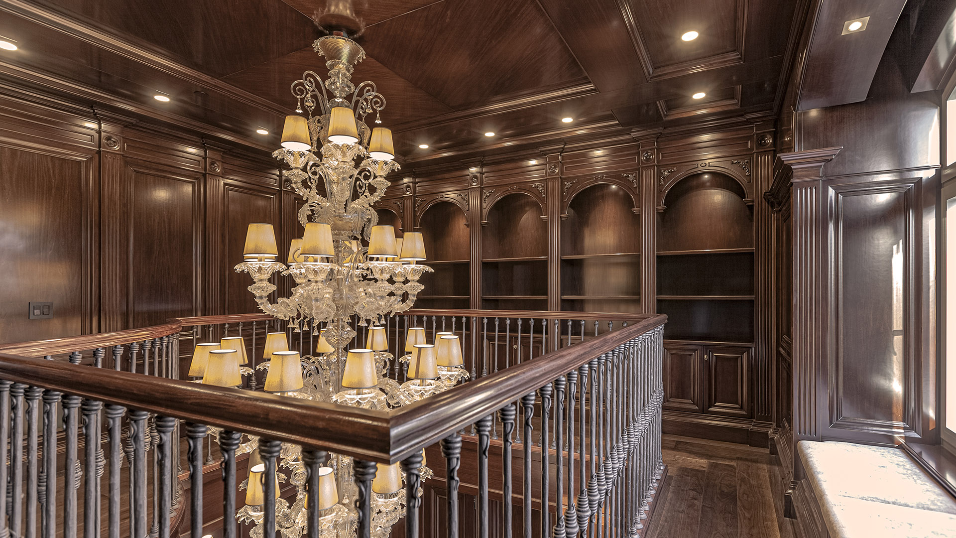 Altamont's Muse upper library mezzanine with chandelier and arched bookcases in West Vancouver
