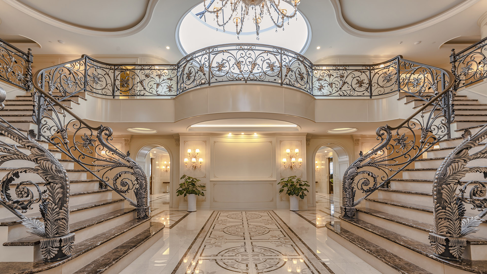Ambleside Palace grand double staircase with hand-forged iron railings and inlaid marble medallion floor in West Vancouver