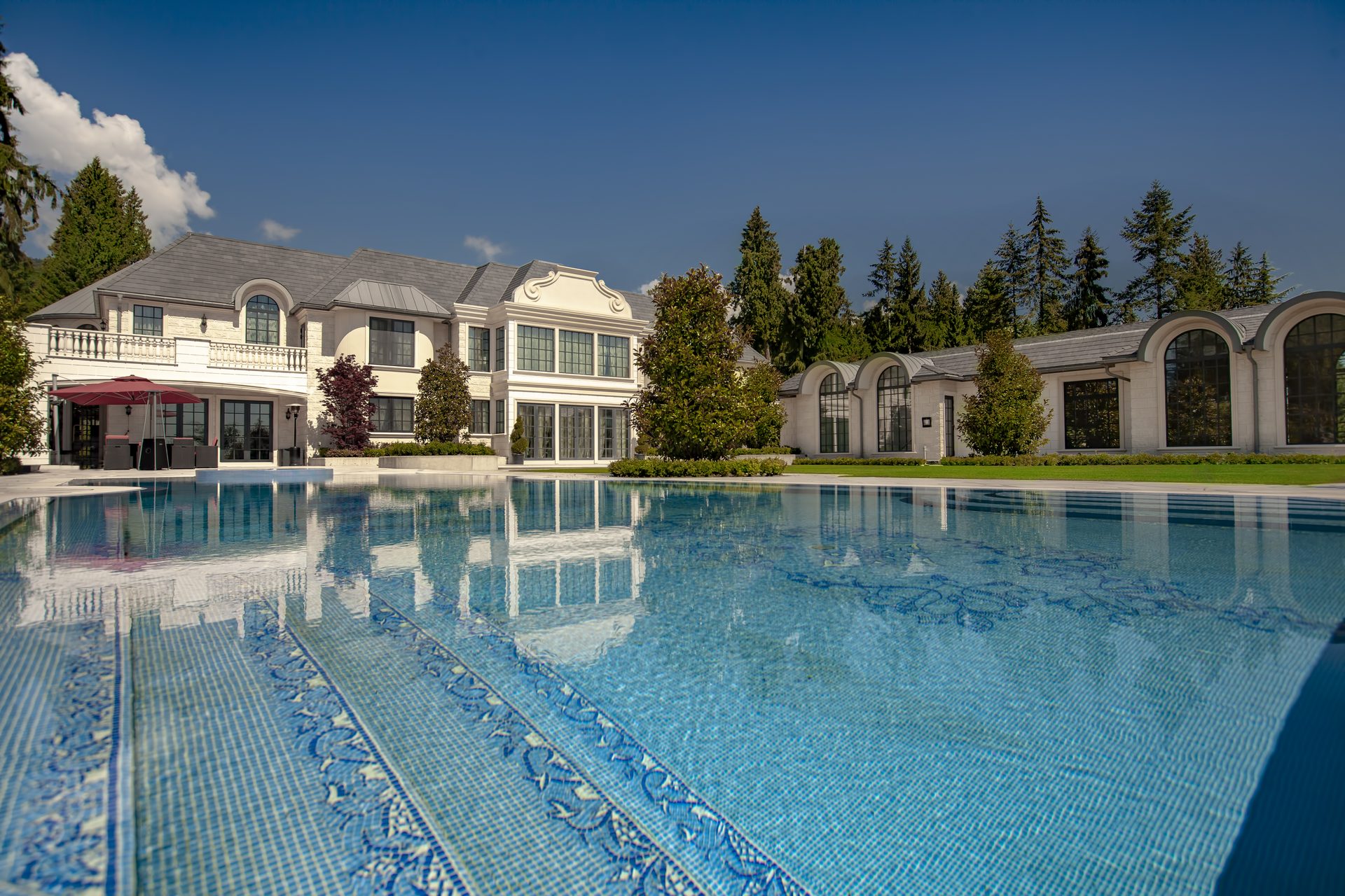Ambleside Palace pool with blue mosaic tile entry steps and covered stone terrace in West Vancouver