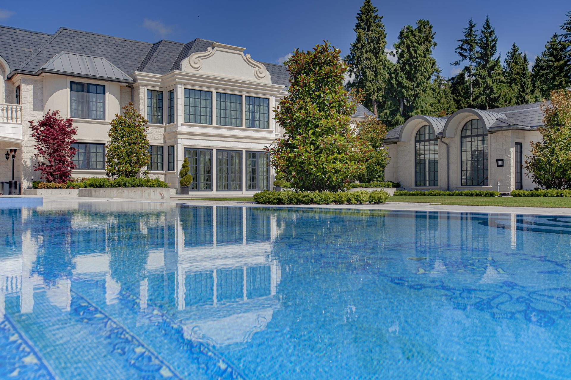 Ambleside Palace classical stone facade reflected in the infinity pool with arched pavilion wing in West Vancouver