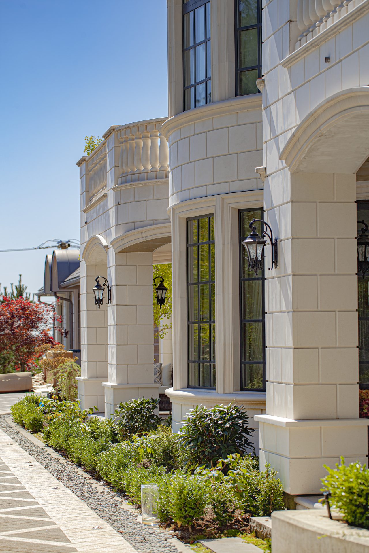 Ambleside Palace side elevation with stone colonnade, iron lanterns, and garden bed in West Vancouver