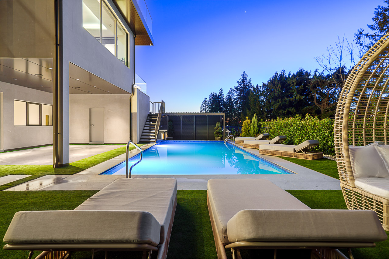 Resort-style pool at dusk with loungers rattan daybed and illuminated water ground level view The Butterfly West Vancouver