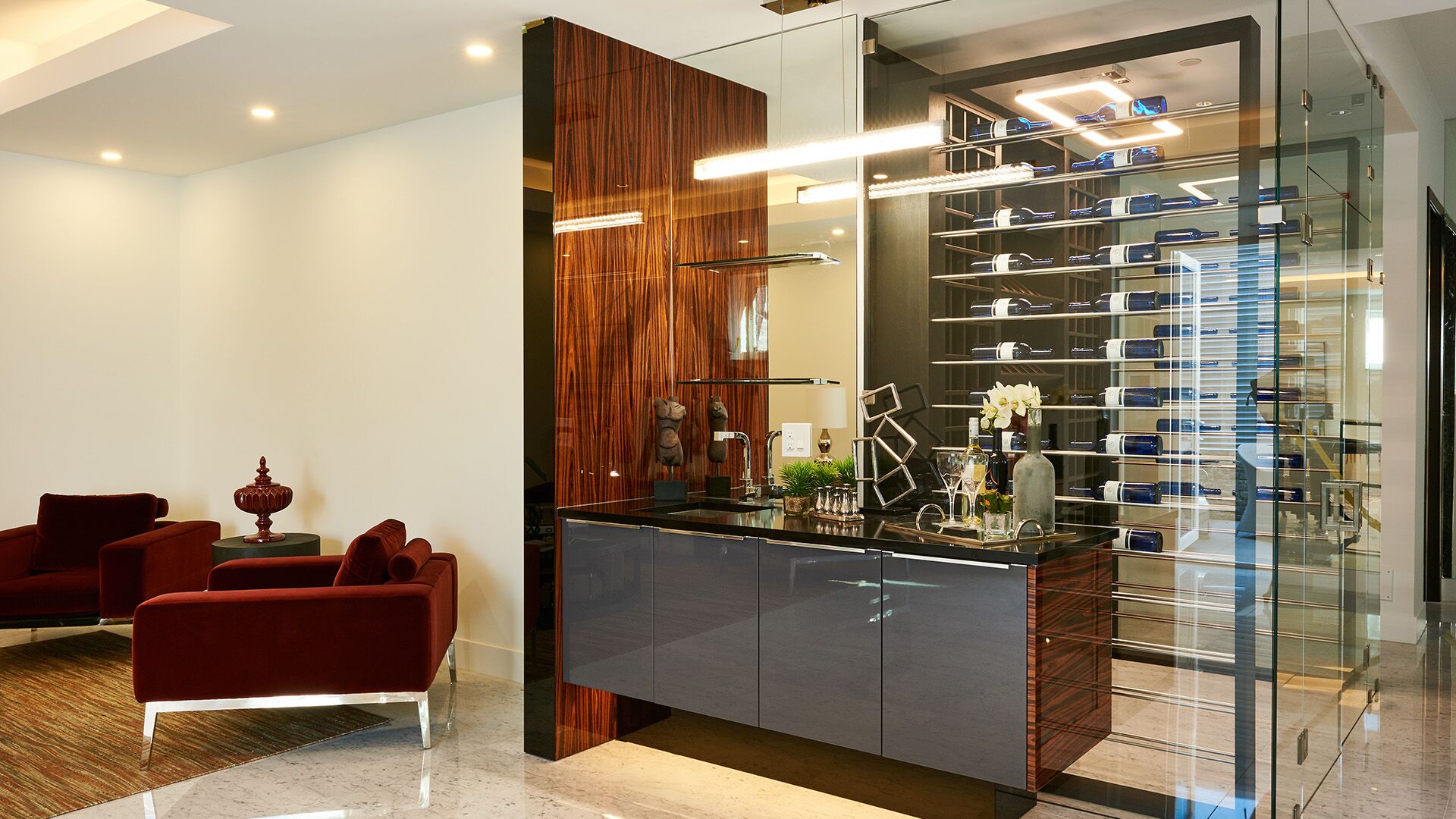 Wine bar and glass-enclosed wine cellar with zebrawood feature panel navy lacquer bar and red velvet armchairs at California Dreams designed and installed by Eurohouse Construction