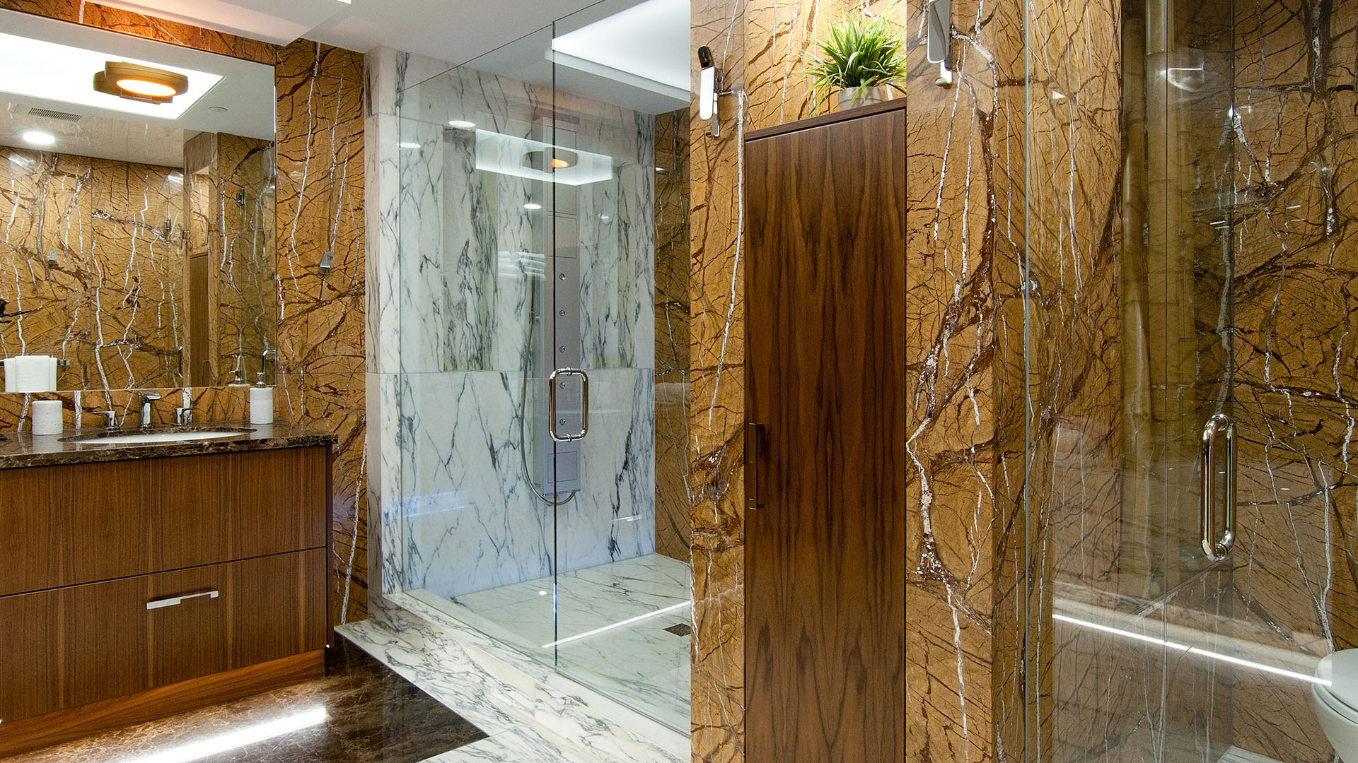 Ensuite bathroom with signature gold Rainforest marble walls frameless glass shower walnut floating vanity and LED under-cabinet lighting Millstream British Properties