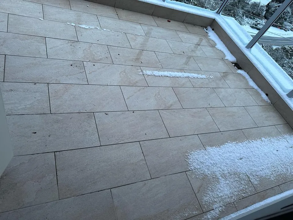 Completed strata balcony deck with new tile surface and electric snow-melt system in North Vancouver — deck stays clear while snow gathers at the edges