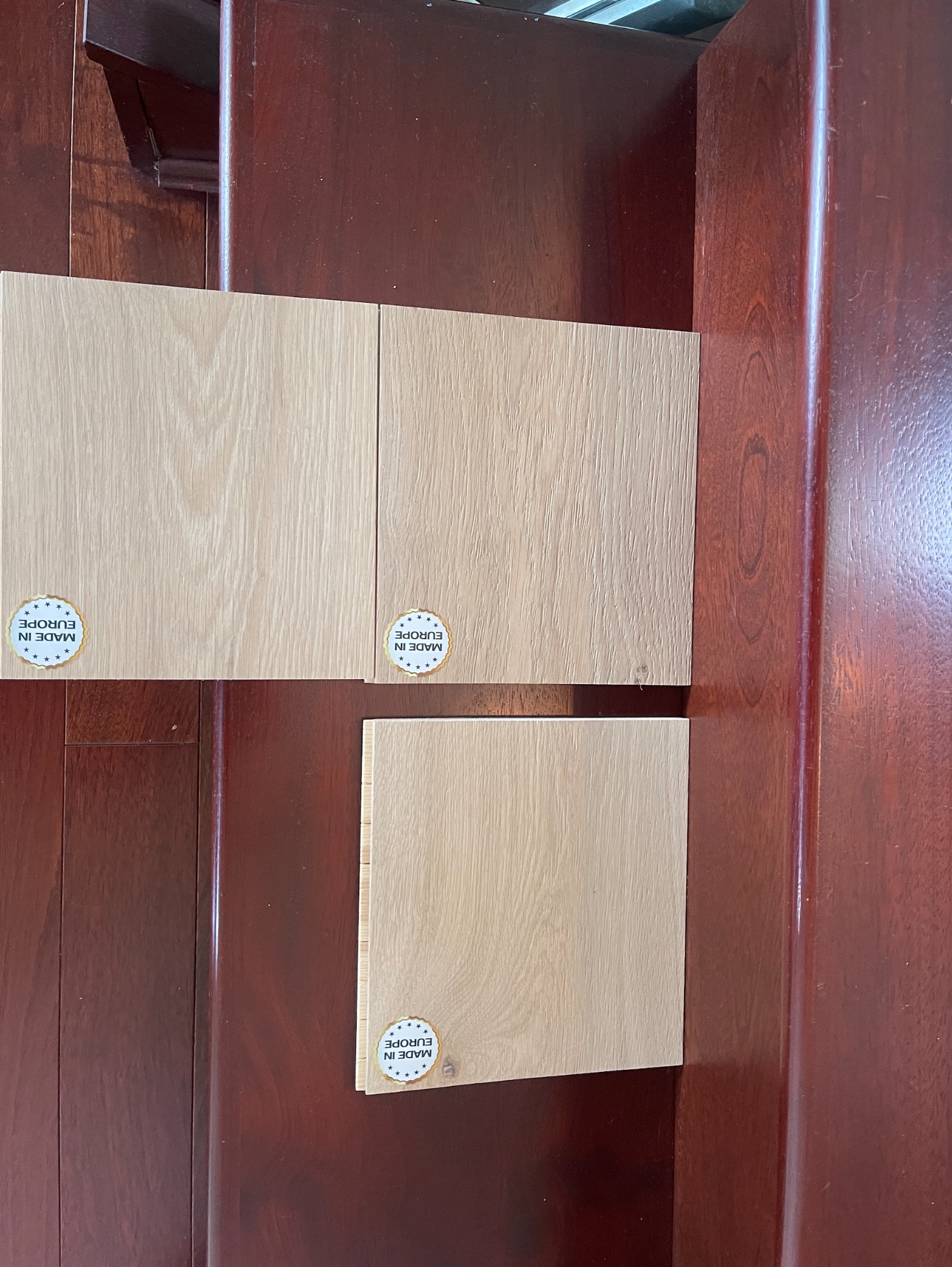 European oak replacement hardwood samples placed on original deep red hardwood stairs at Newdale Court showing colour mismatch that led to full floor replacement approval by Shore Insurance