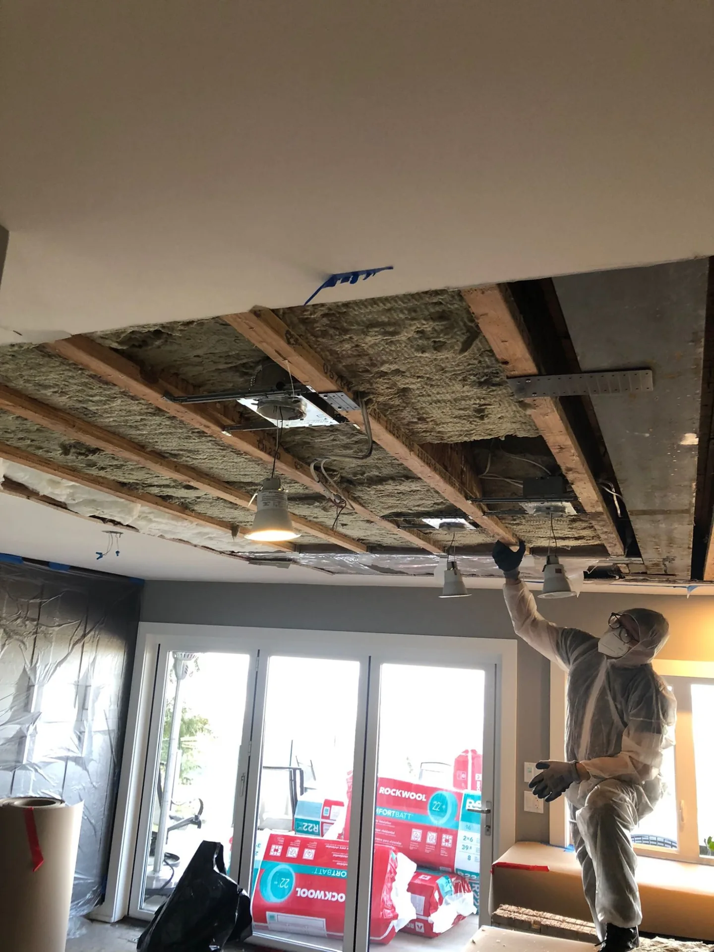 Ceiling opened during strata water damage repair in North Vancouver, exposing floor joists with insulation staged for reinstallation — what an envelope line item can look like in construction