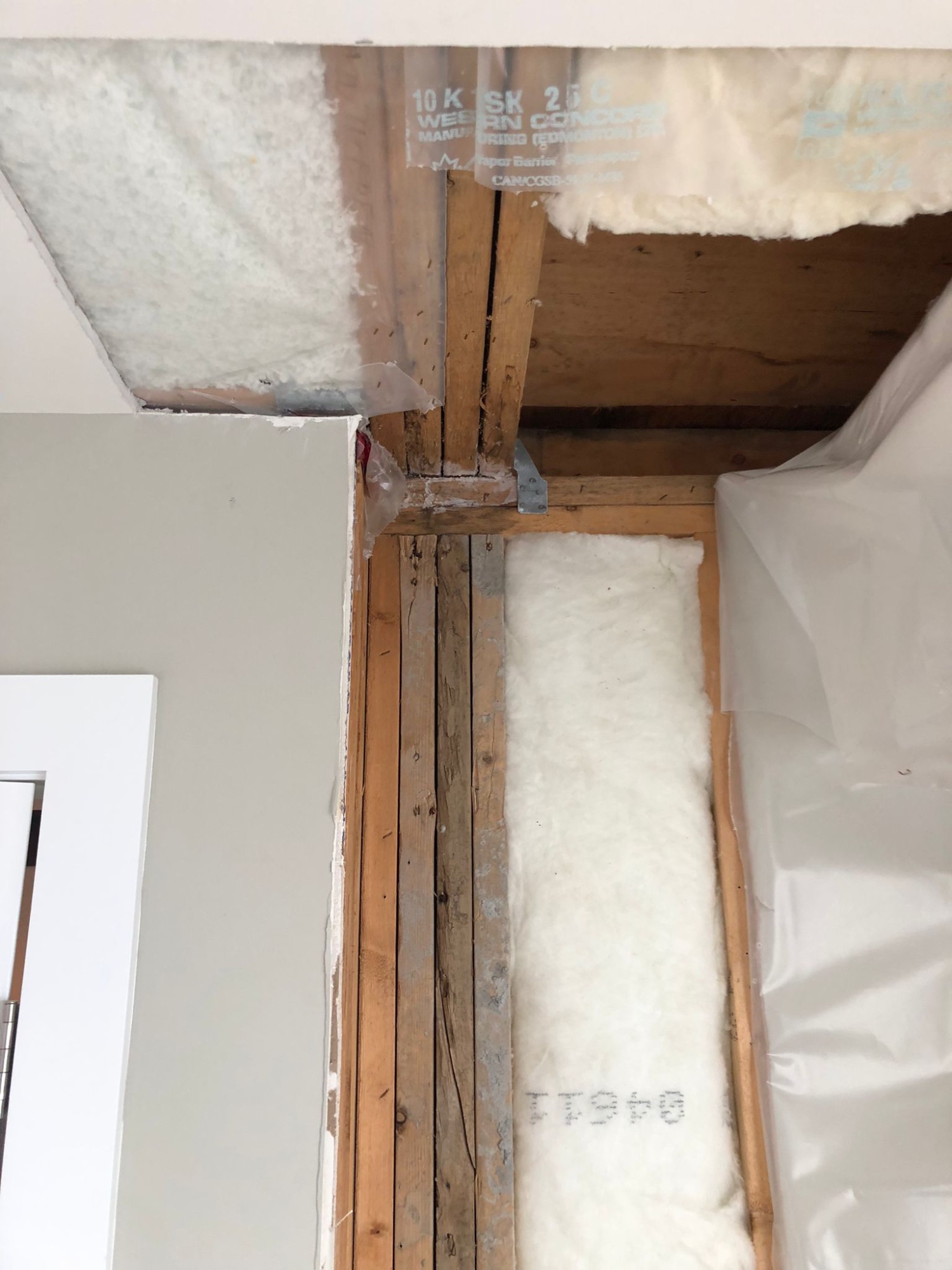 Exterior wall opened from floor to ceiling at Newdale Court showing framing and new fiberglass insulation being installed during structural repair