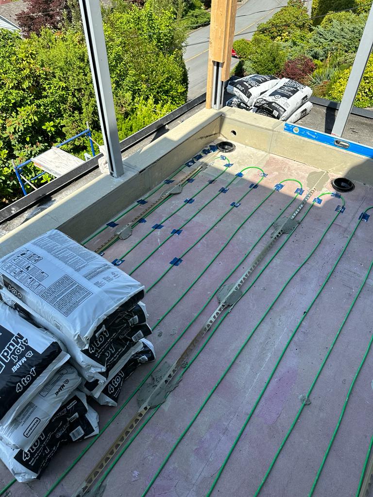 Wide view of balcony deck at Newdale Court showing electric snow melter cable layout with drain penetrations and spirit level for slope verification