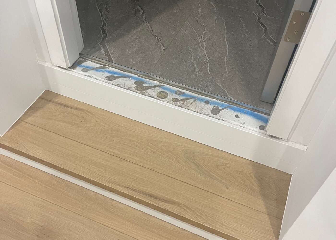 New laminate flooring meeting tile at doorway threshold with professional transition strip — detail of quality floor installation after subfloor levelling