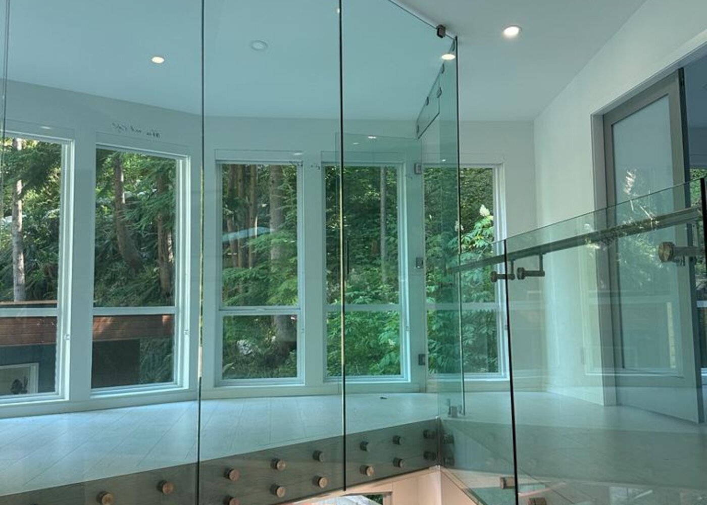 Double-height glass railing and window wall in luxury North Vancouver home with views of trees — before winter storm water damage through skylights