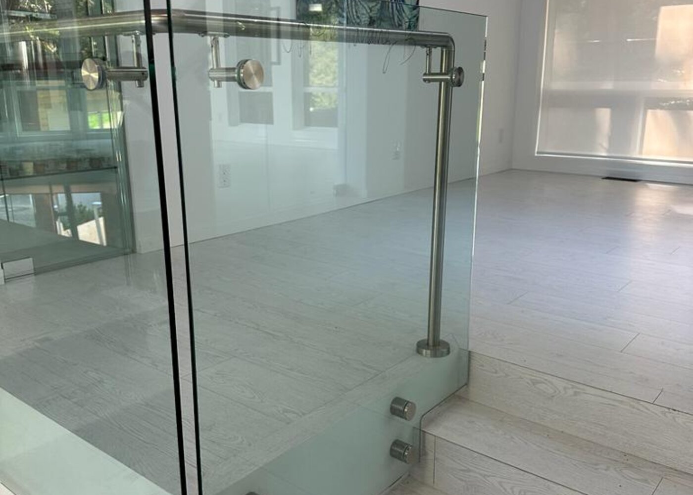 Glass railing detail at stair landing with existing light wood flooring in North Vancouver home before insurance restoration