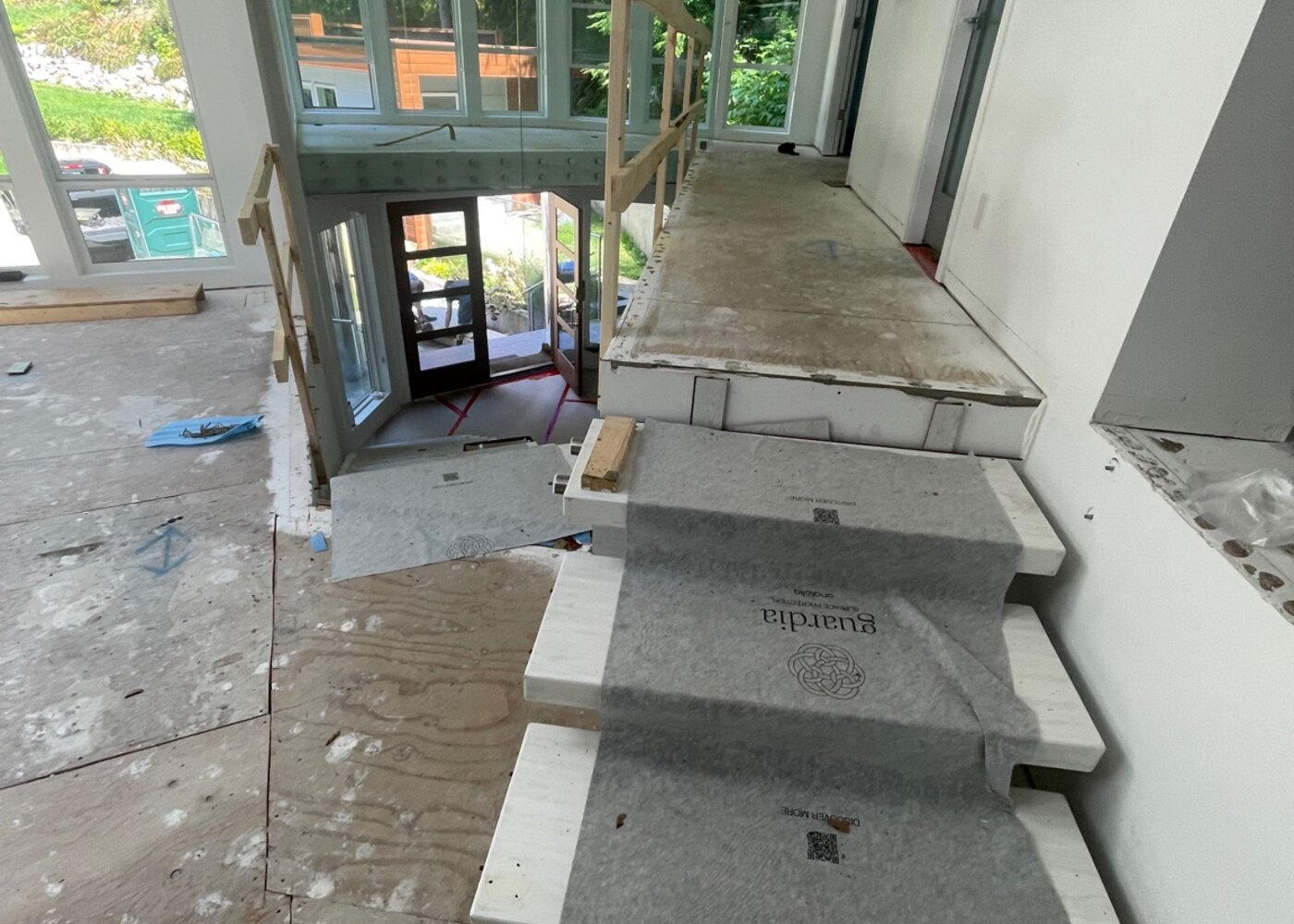 New stair treads being installed with surface protection covering in place and glass railing system visible during flooring restoration