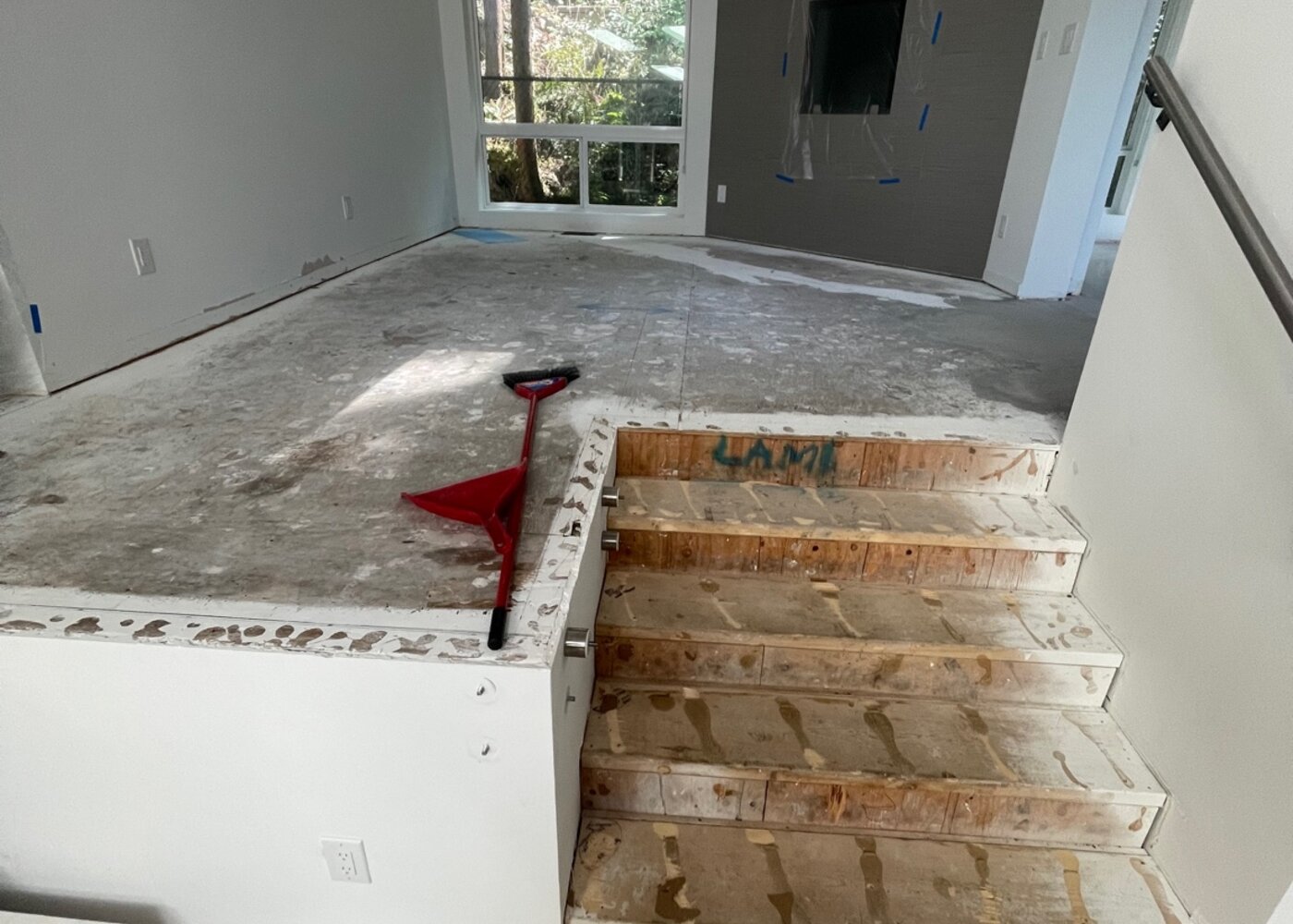 Upper level view showing stripped subfloor with exposed stair stringers, red scraper tool, and living room with fireplace feature wall during restoration