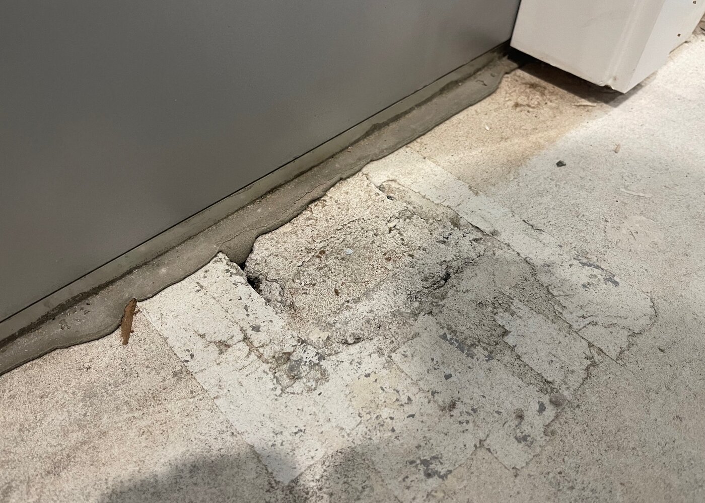 Crumbling concrete subfloor with holes and deterioration exposed after water-damaged laminate removal during insurance restoration in North Vancouver