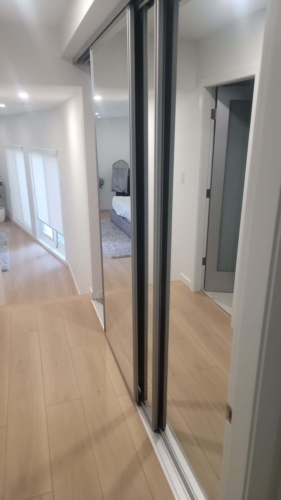 Hallway with new laminate flooring and full-height mirrored closet doors reflecting bedroom at Prospect Road North Vancouver by Eurohouse Construction