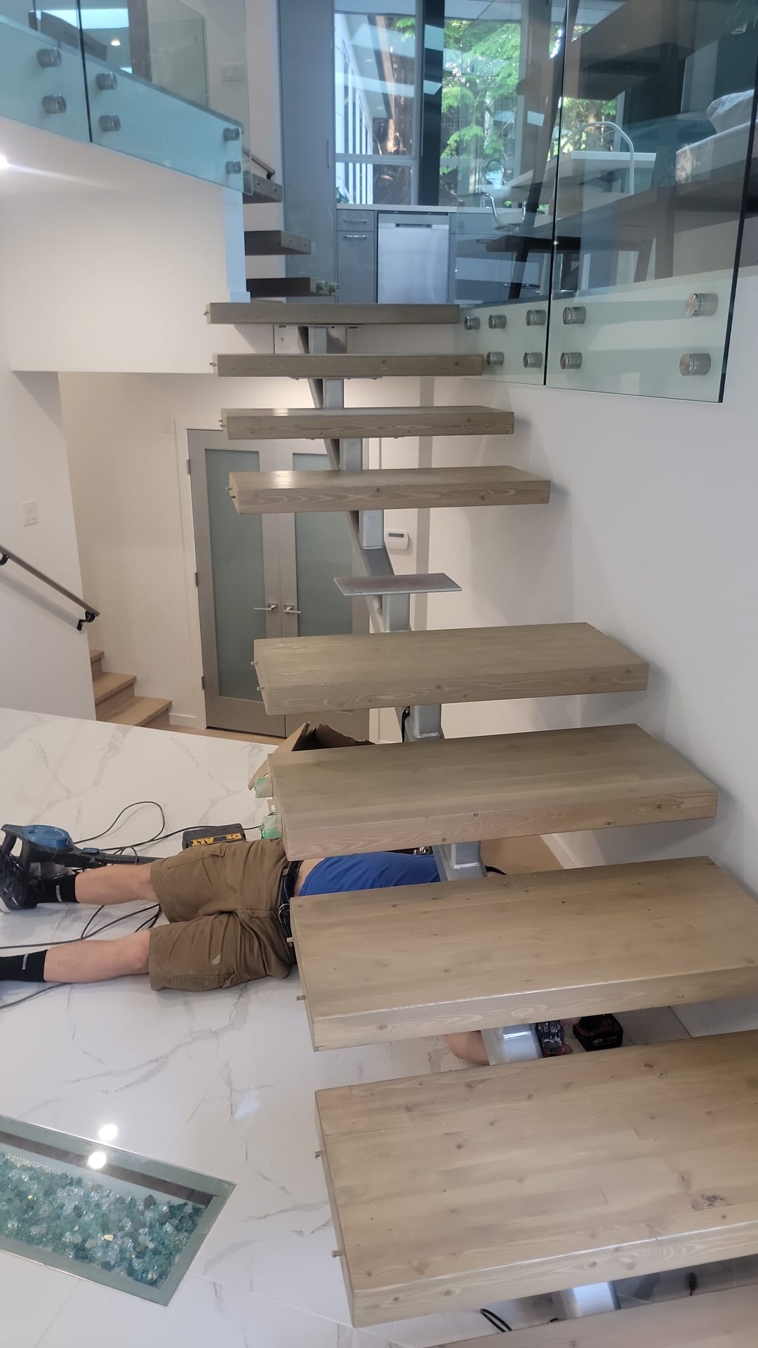 Carpenter installing floating wood stair treads on steel mono-stringer with glass railing at Prospect Road North Vancouver by Eurohouse Construction