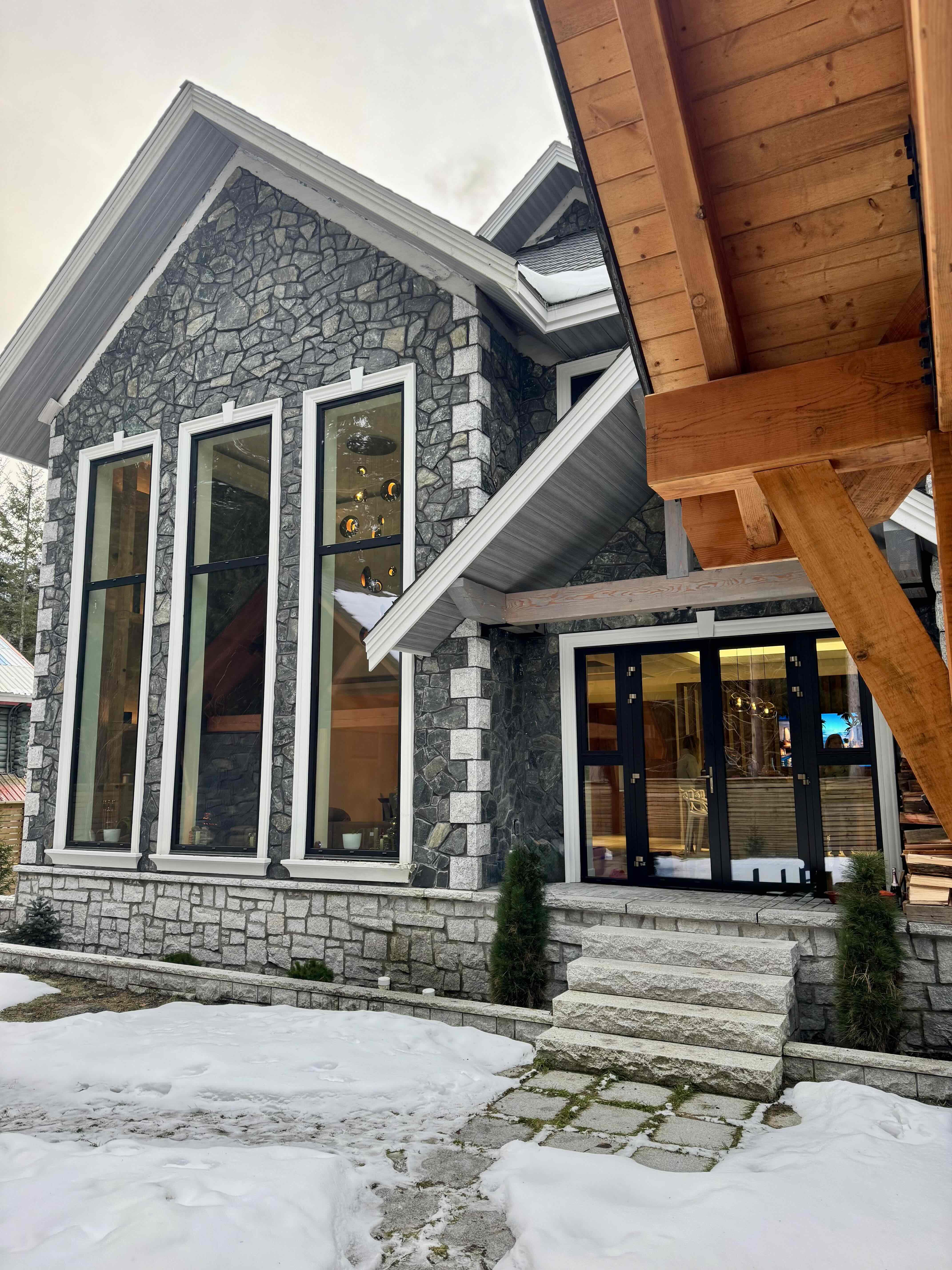 Rear exterior of Rainbow in Whistler showing stone facade, floor-to-ceiling windows, and timber gazebo pavilion — custom home by Eurohouse Construction