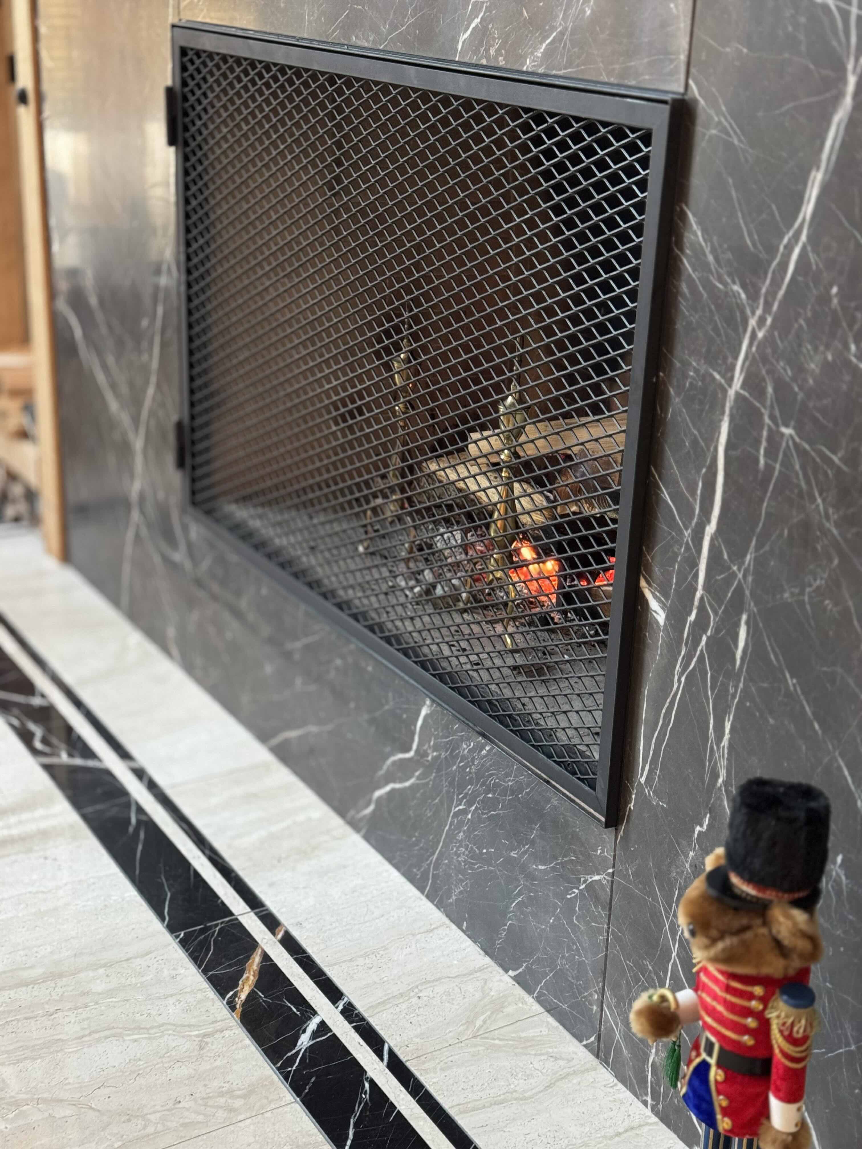 Marble fireplace close-up showing multi-tone stone inlay and mesh fire screen at Rainbow in Whistler luxury home by Eurohouse Construction