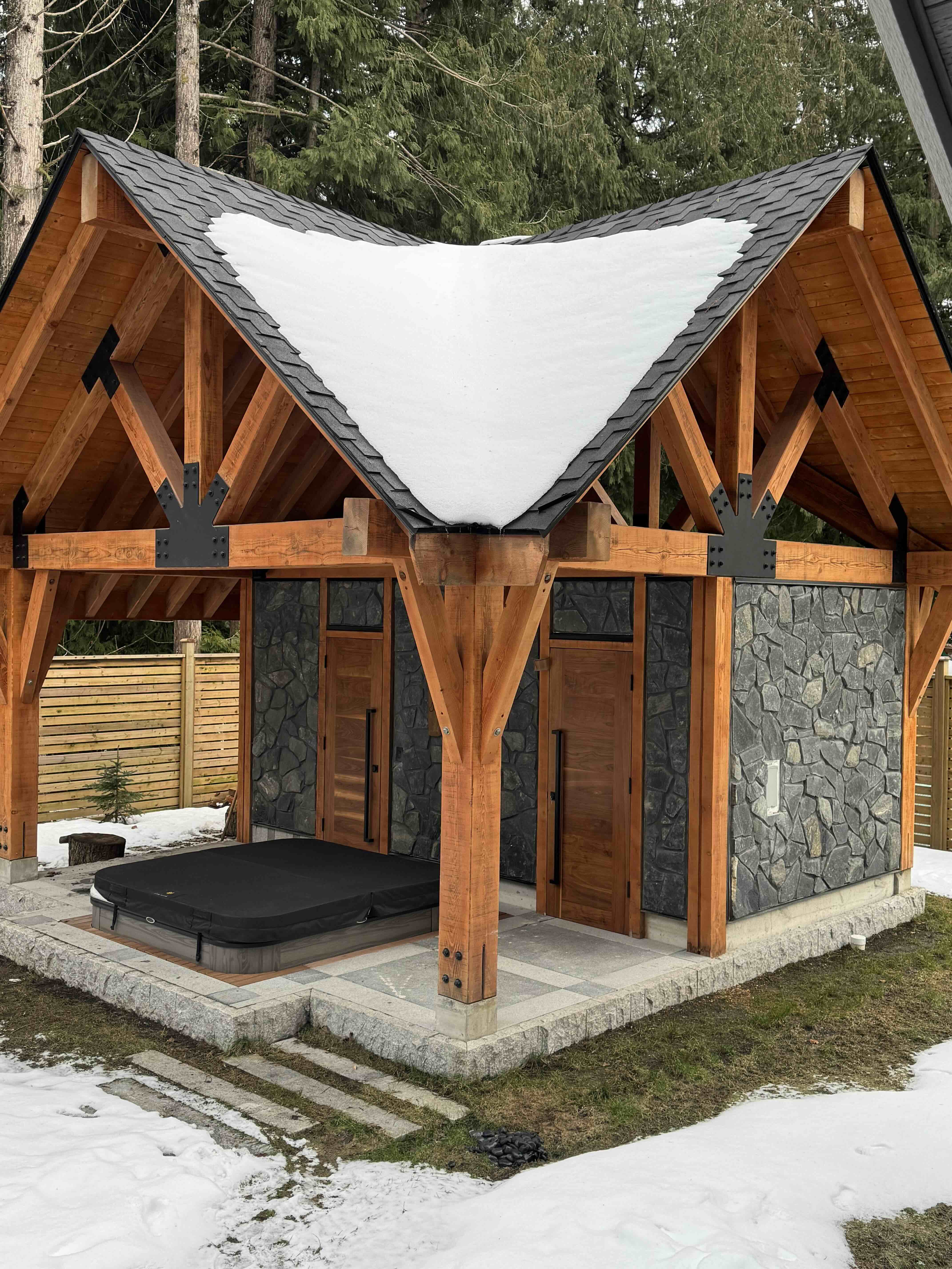 Custom timber-frame gazebo with hot tub, steel bracket joinery, and stone walls at Rainbow in Whistler luxury home by Eurohouse Construction