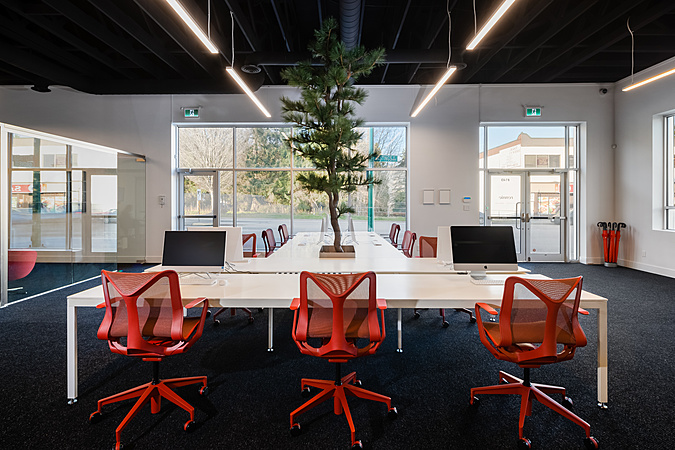 Completed Rennie open-plan office interior with exposed ceiling, linear lighting, and red Cosm chairs — built by Eurohouse Construction West Vancouver