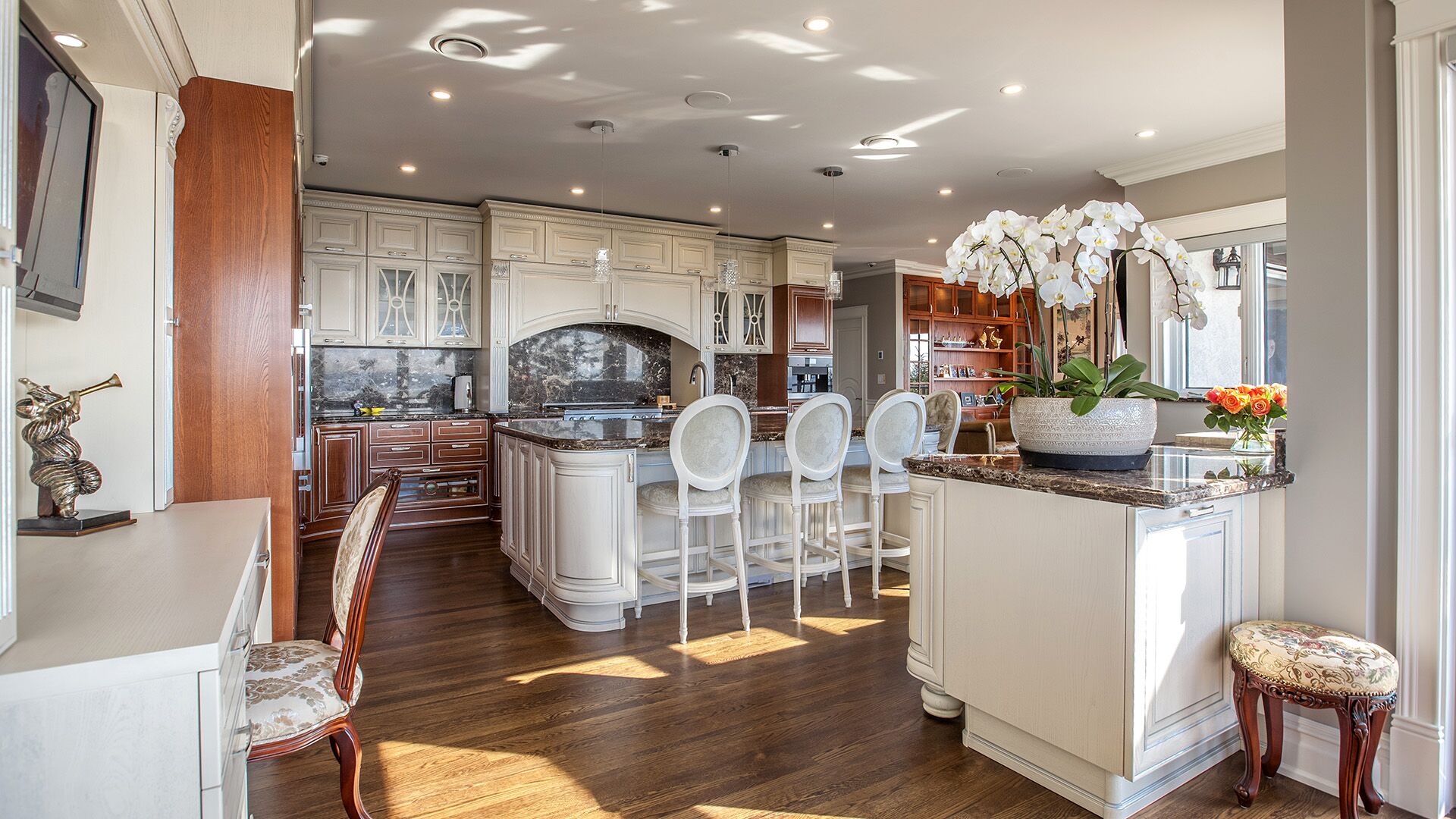 Kitchen from breakfast nook showing full breadth of cream cabinetry cherry wood accents orchid arrangement and cherry panelled family room beyond at Rockridge Classic built by Eurohouse Construction