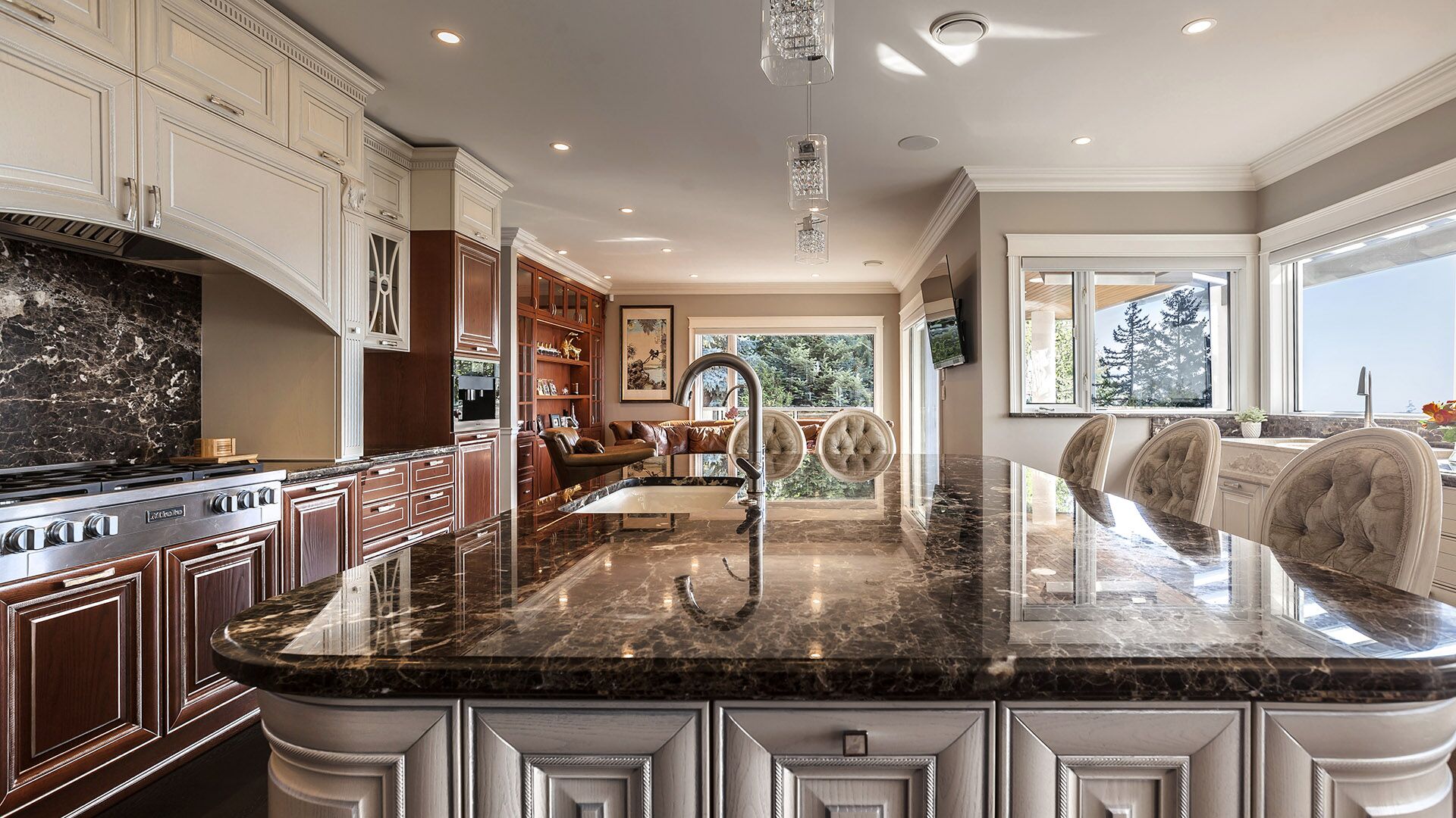 Low angle of Emperador Dark marble kitchen island showing polished surface gooseneck faucet cream raised-panel base and cherry panelled family room beyond at Rockridge Classic built by Eurohouse Construction