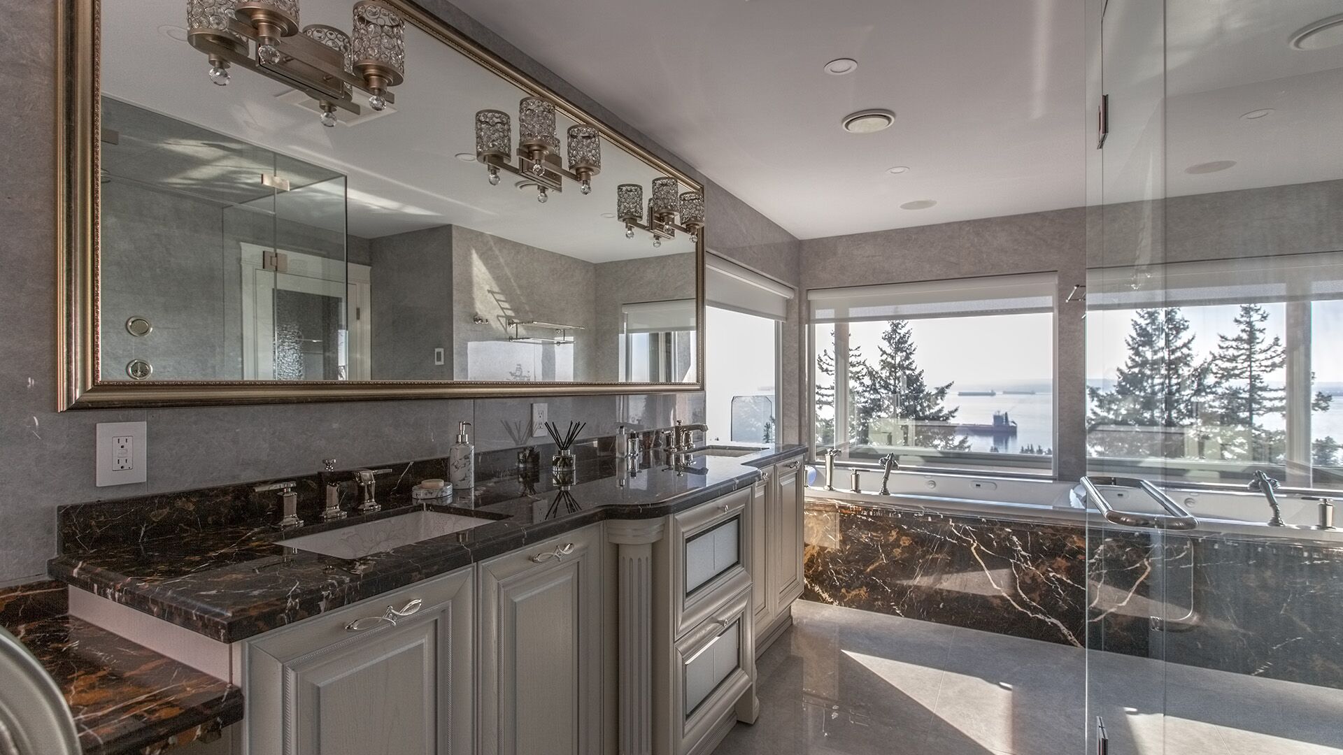 Double vanity with Emperador Dark marble countertop framed mirror crystal sconces silver textured wallcovering and ocean view soaking tub at Rockridge Classic built by Eurohouse Construction