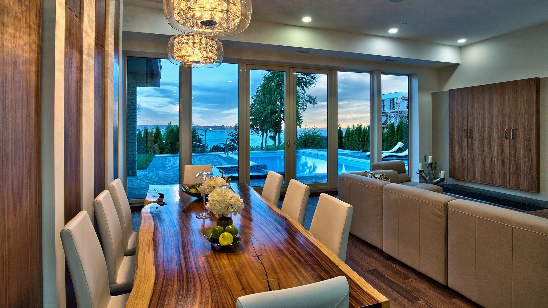 Live-edge walnut dining table with crystal chandelier and pool views at Rose Crescent Sandy Cove West Vancouver by Eurohouse Construction