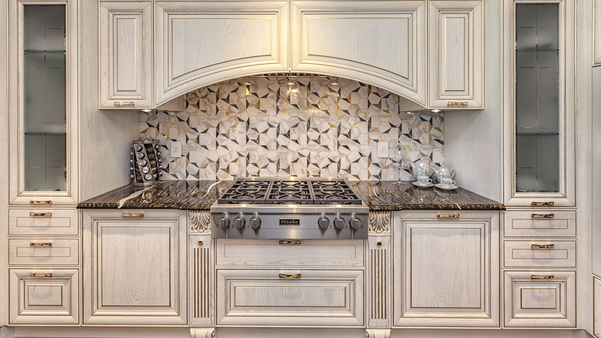 Close-up of Italian classical range wall with geometric gold and marble mosaic backsplash, carved corbels, and Miele cooktop by Eurohouse Construction West Vancouver