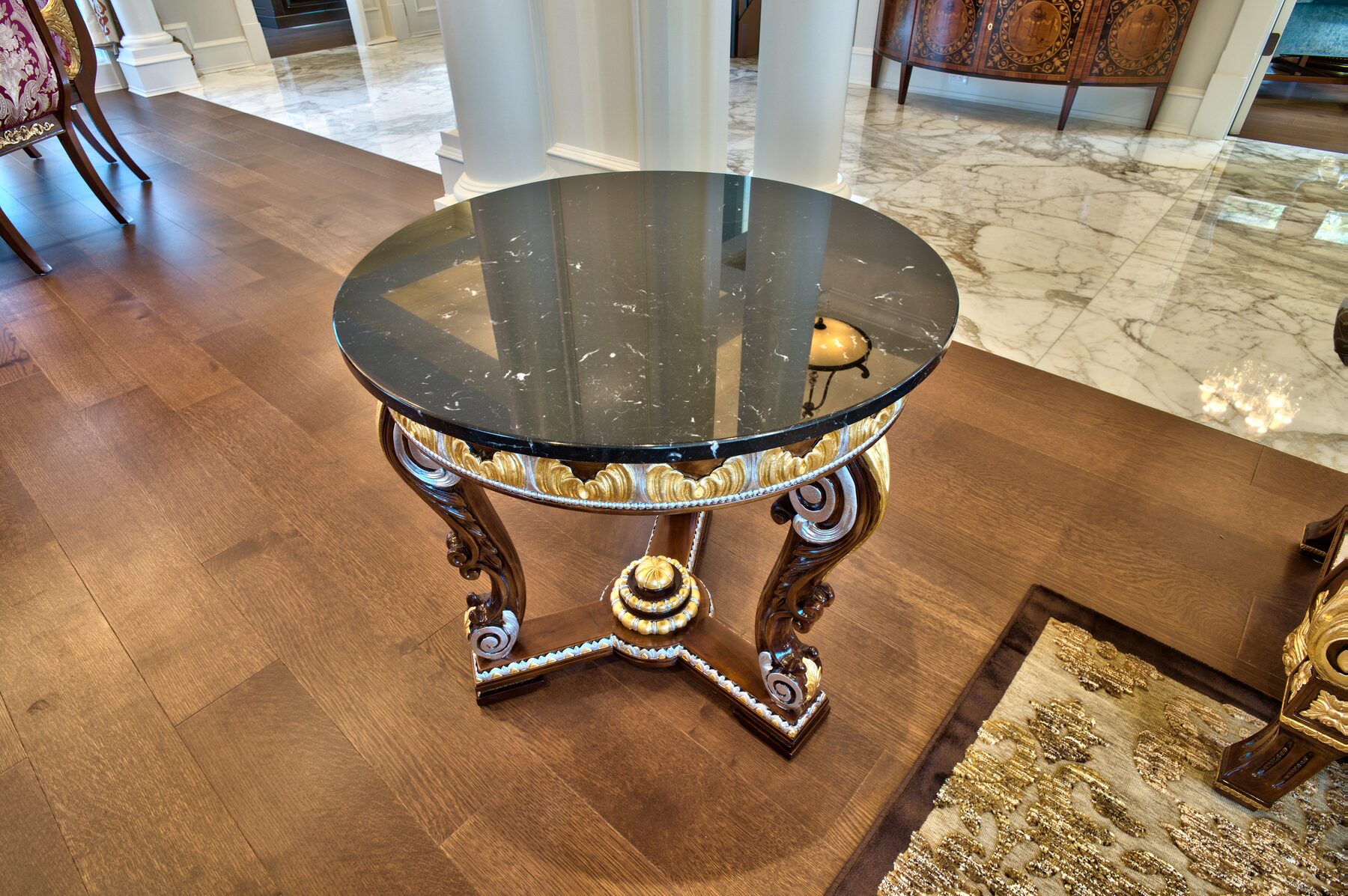 Round glass topped Francesco Molon table on a heavily carved and gilded tripod base on a hardwood floor in a Vancouver home furnished by Eurohouse Construction