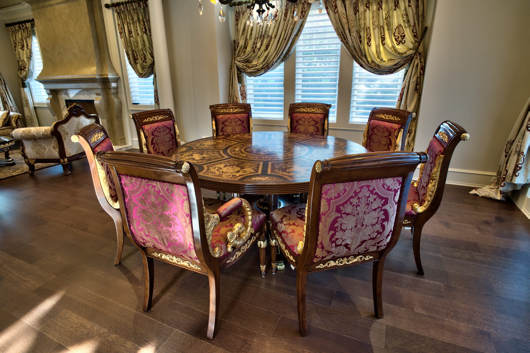 Wide view of a formal dining room with inlaid round Francesco Molon table and carved damask chairs beneath a chandelier in a Vancouver home furnished by Eurohouse Construction