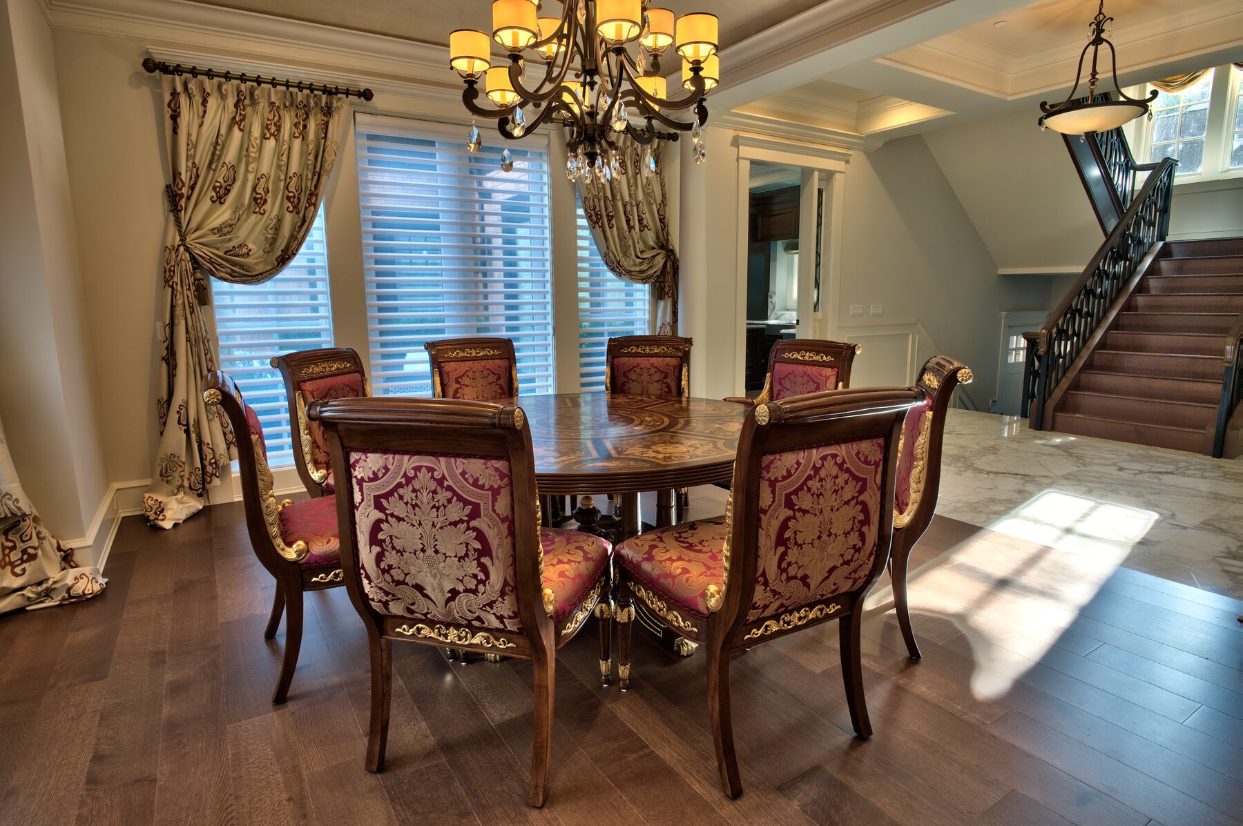 Formal dining room with a round inlaid Francesco Molon table, carved chairs in crimson and gold damask, crystal chandelier, and gold drapery in a Vancouver home furnished by Eurohouse Construction
