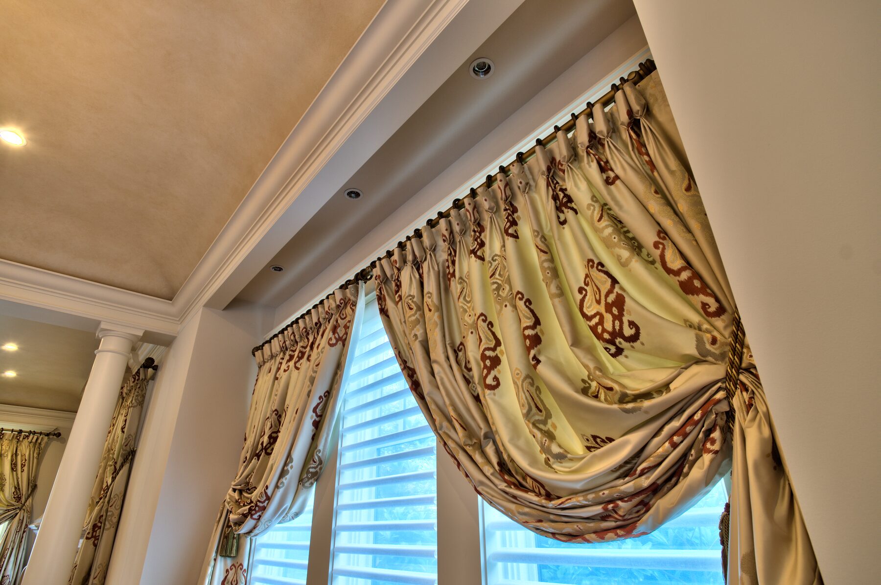 Swagged and tailed gold drapery treatment above a tall window between columns in a Vancouver home furnished by Eurohouse Construction