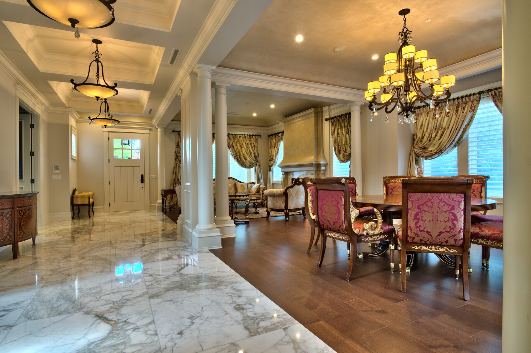 Long interior view across marble and hardwood floors to a chandelier lit dining room with carved Italian furniture in a Vancouver home furnished by Eurohouse Construction