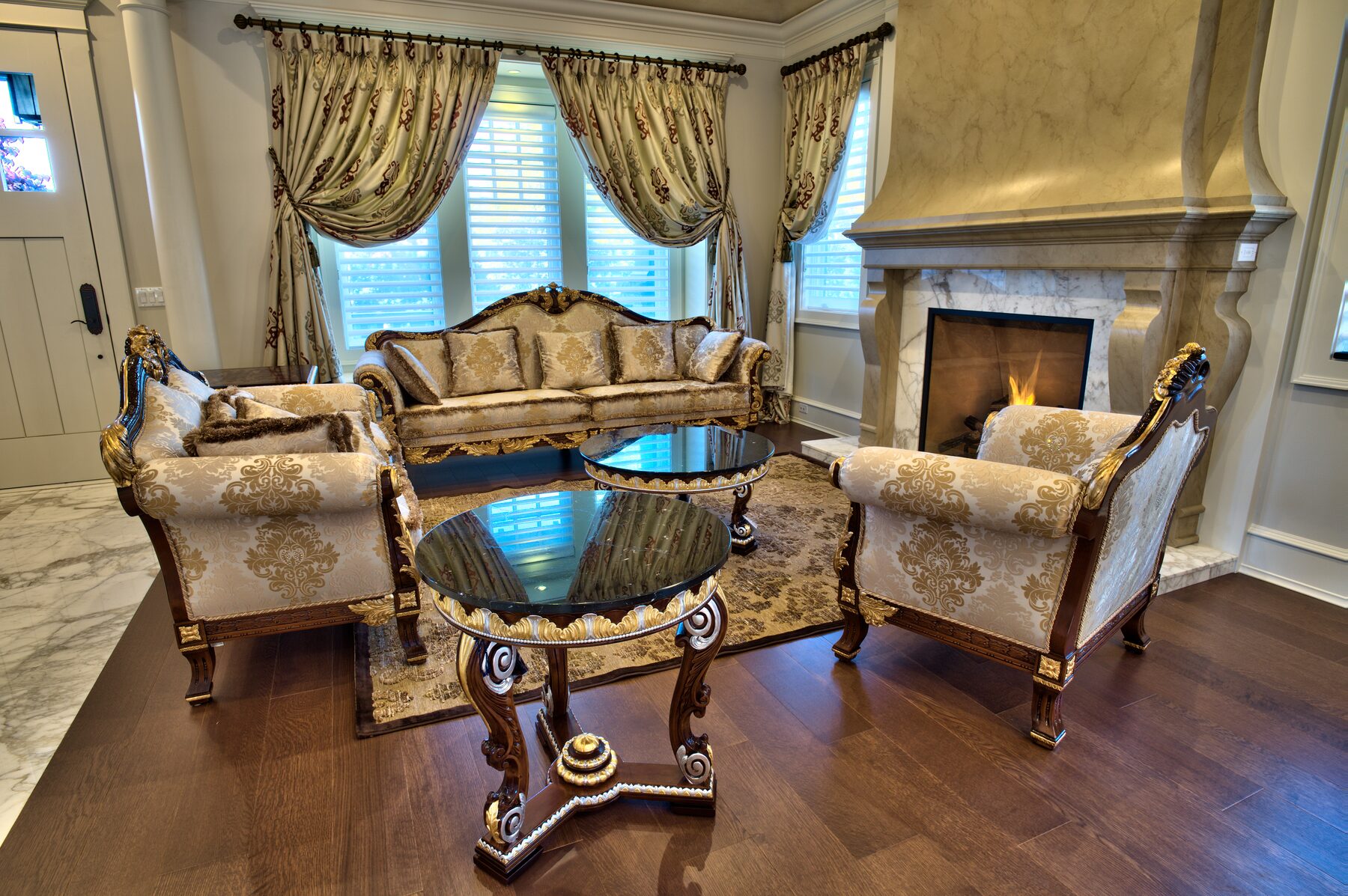 Carved armchairs and glass topped Francesco Molon table with gilded base in front of a marble fireplace, Italian furniture installed by Eurohouse Construction in Vancouver