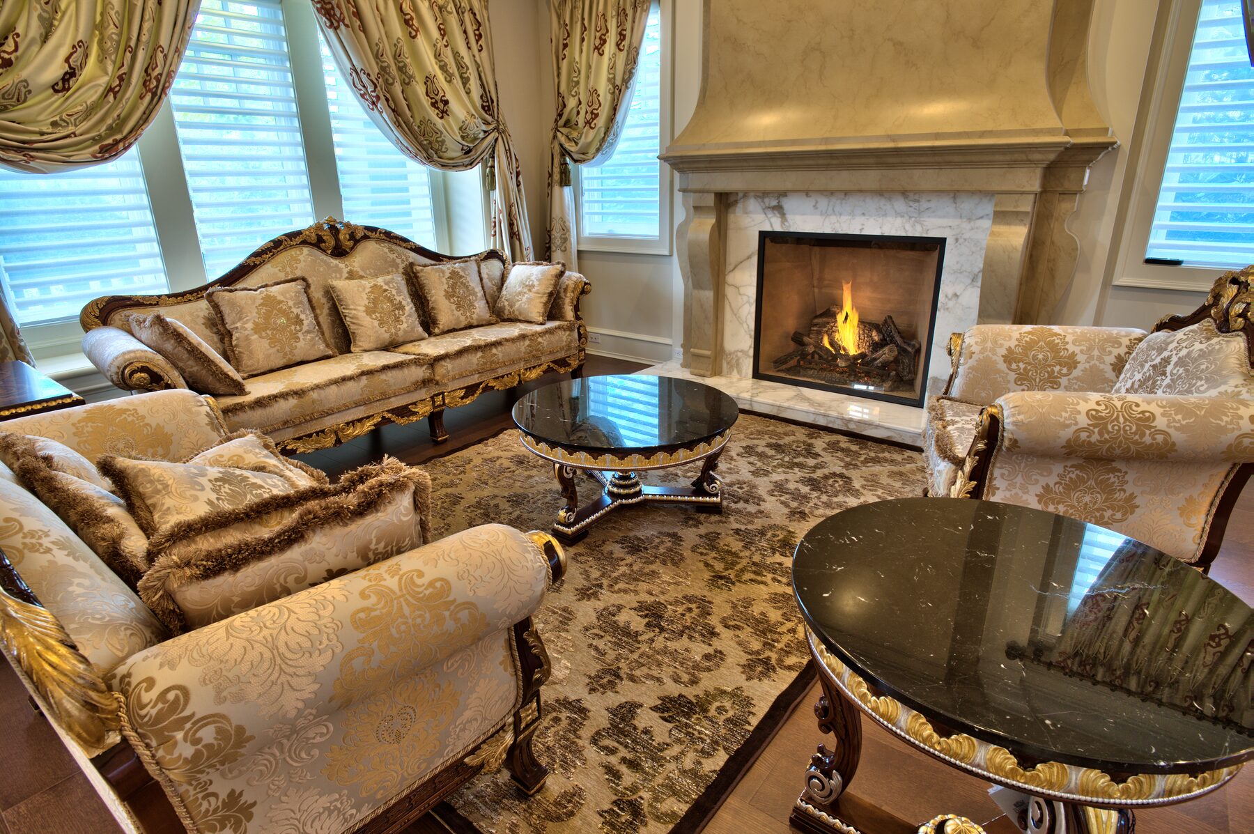 Living room seating group with carved Francesco Molon sofa, armchairs, and oval glass topped table beside a lit fireplace in a Vancouver home furnished by Eurohouse Construction