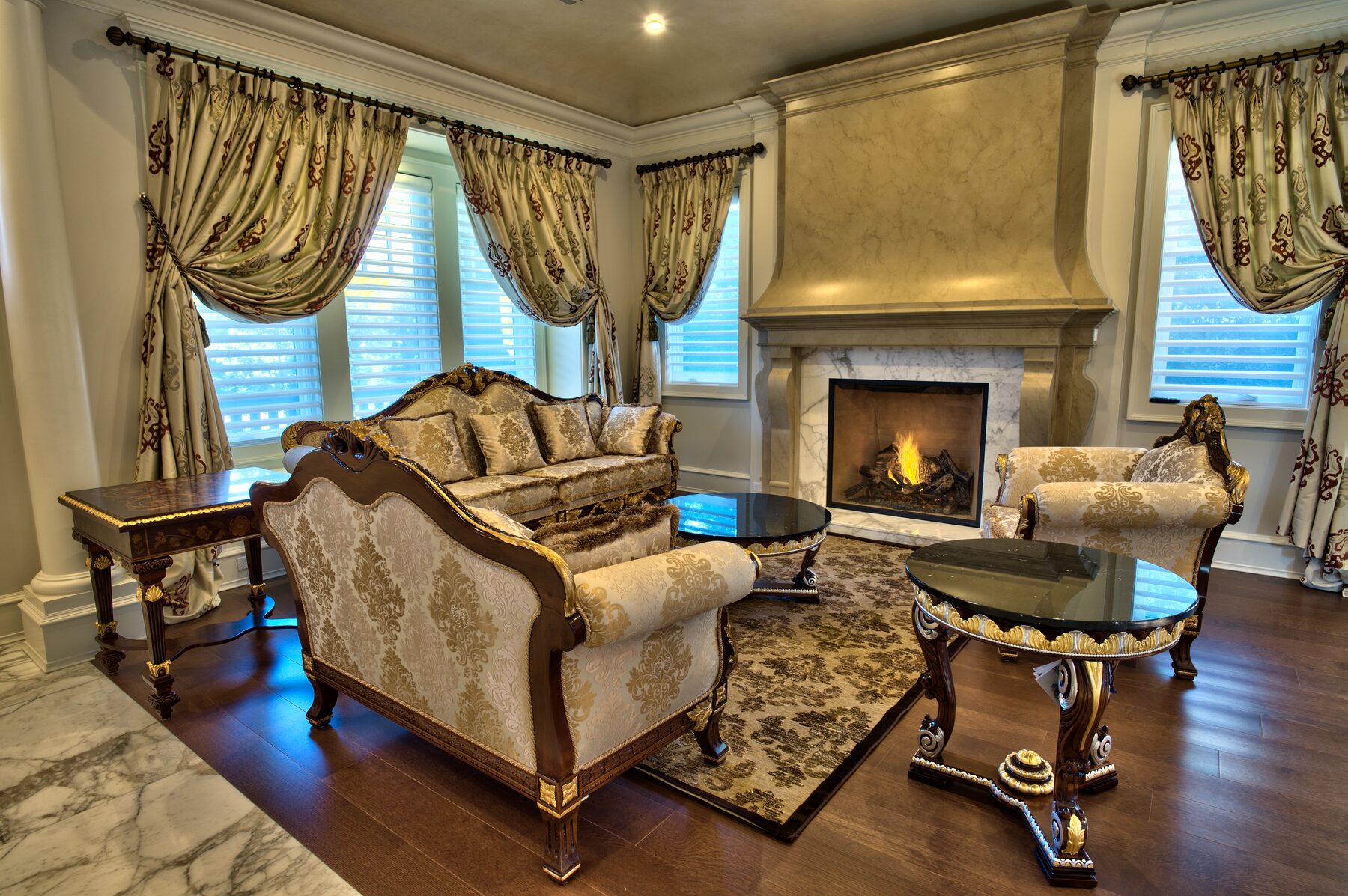 Pair of carved Francesco Molon settees in silk damask facing a lit fireplace with marble surround and layered gold drapery in a Vancouver living room furnished by Eurohouse Construction
