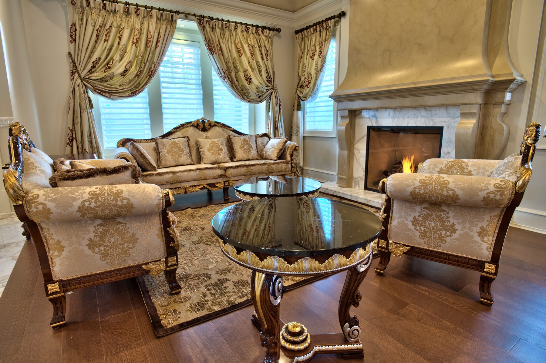 Wide view of a living room with carved Italian settees, marquetry centre table, and lit fireplace in a Vancouver home furnished by Eurohouse Construction