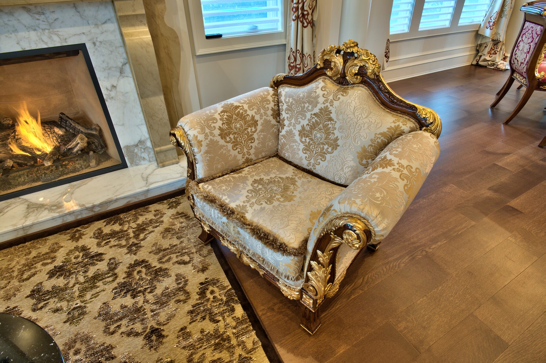Carved Francesco Molon loveseat in cream and gold damask beside a lit marble fireplace in a Vancouver living room furnished by Eurohouse Construction