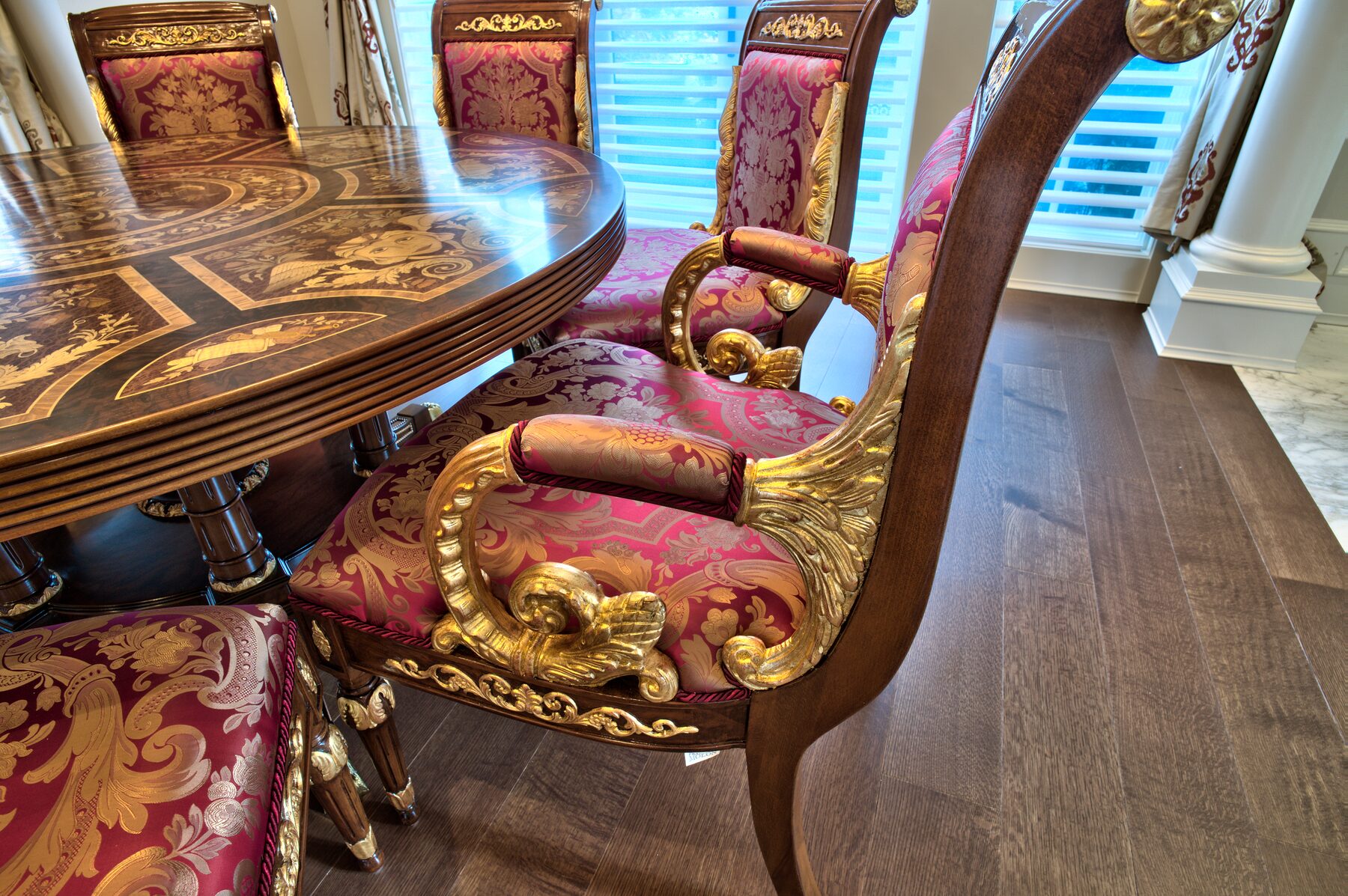 Carved and gilded Francesco Molon dining chair with crimson damask upholstery beside an inlaid round table in a Vancouver home furnished by Eurohouse Construction