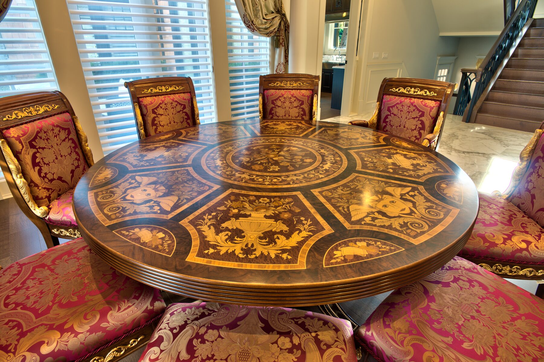 Detail of radial wood inlay pattern on a Francesco Molon round table surrounded by crimson and gold damask dining chairs in a Vancouver home furnished by Eurohouse Construction