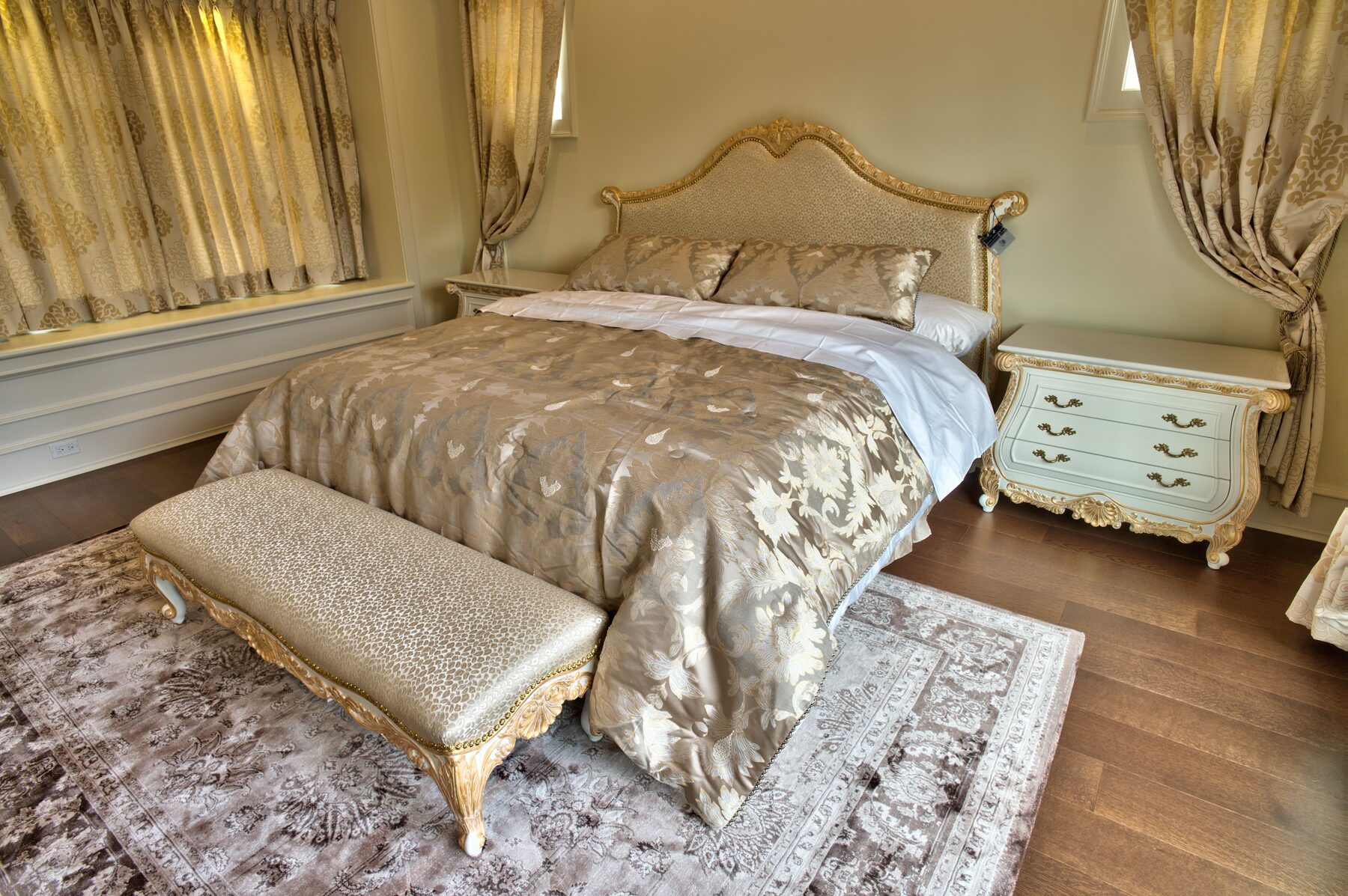 Carved gilded bed with silk coverlet, painted Francesco Molon nightstand, and upholstered bench in a Vancouver primary bedroom furnished by Eurohouse Construction