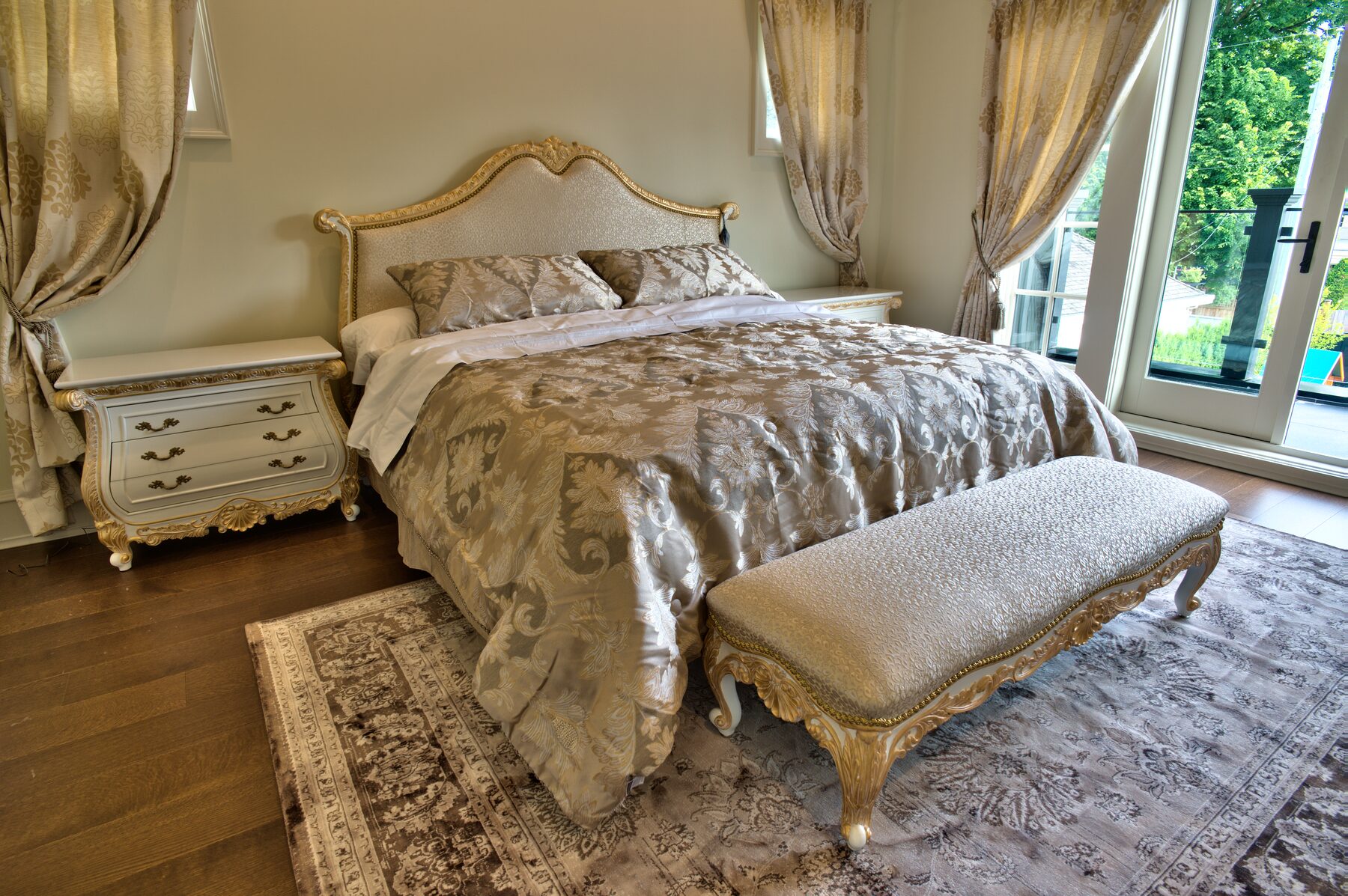 Primary bedroom with a carved and gilded Francesco Molon bed, painted nightstands, upholstered bench, and gold drapery in a Vancouver home furnished by Eurohouse Construction