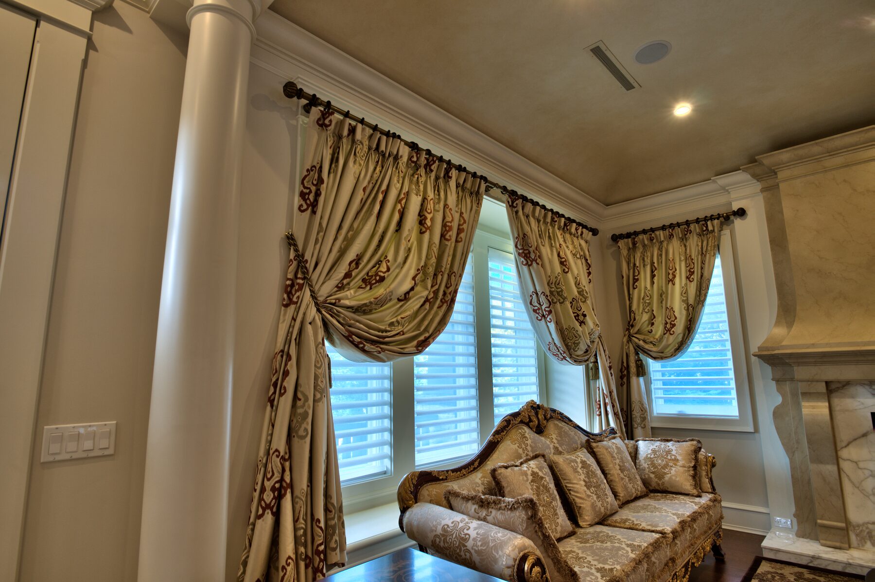 Carved settee beneath full height gold drapery between white columns in a Vancouver home furnished by Eurohouse Construction