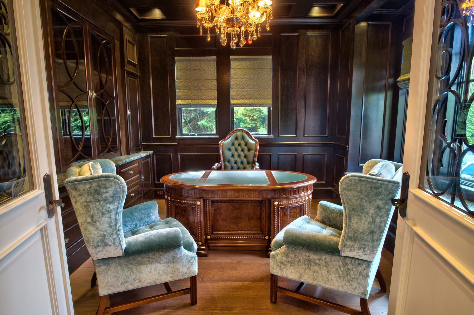 Wood panelled study with a Francesco Molon bowfront desk, tufted leather chair, and pale blue velvet armchairs in a Vancouver home furnished by Eurohouse Construction
